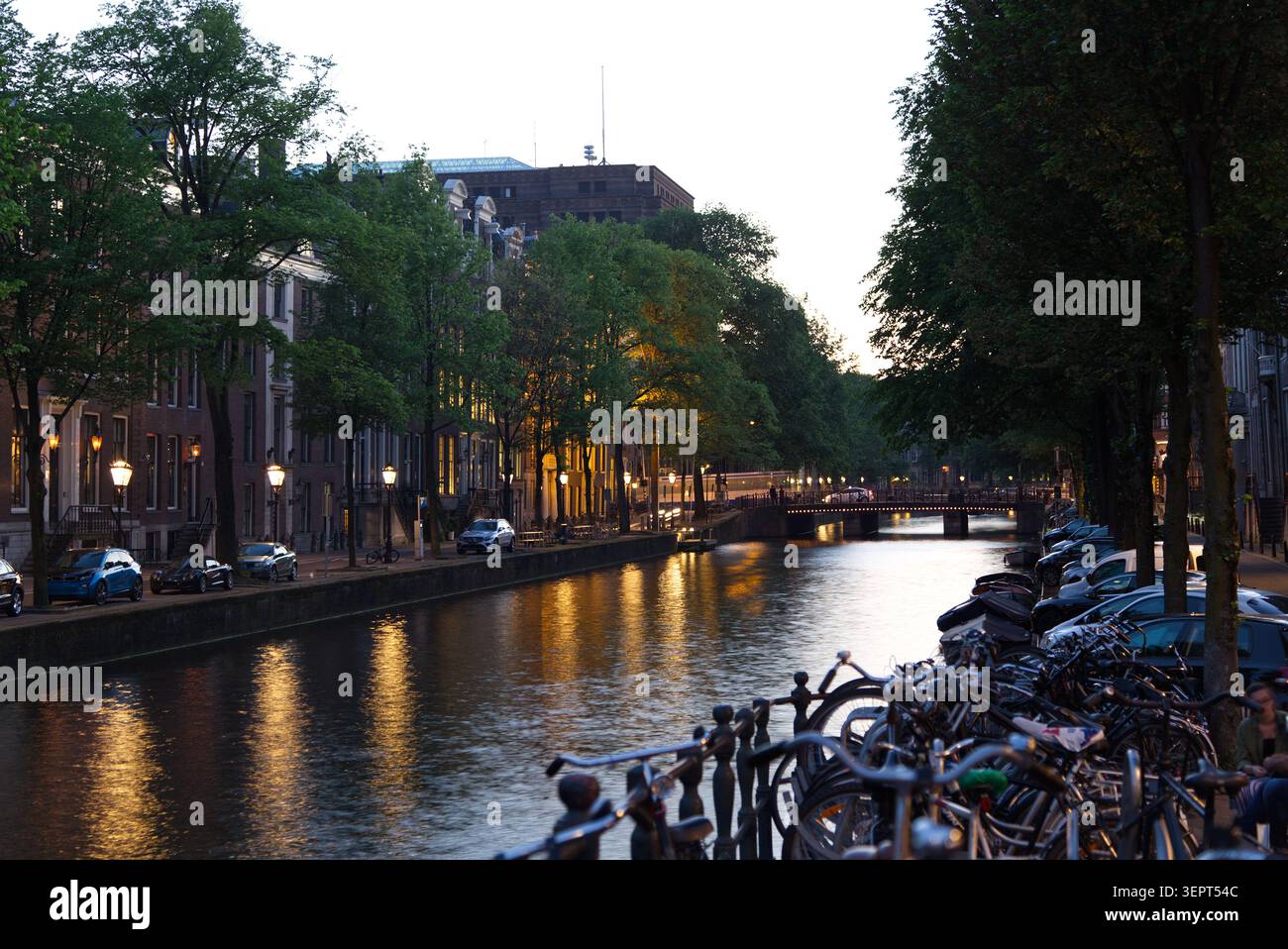 Amsterdamer Kanal in der Abenddämmerung am Sommertag. Eine längere Belichtungszeit erzeugt sanfte atmosphärische Reflexionen im Wasser und sorgt so für eine entspannte Szene. Stockfoto
