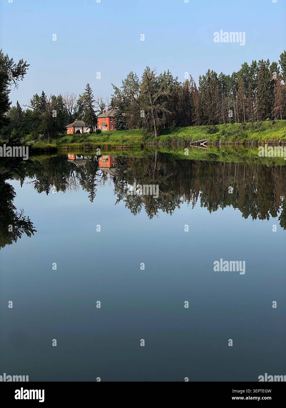 Ruhiges Flusswasser, das gemütliche Häuser und weiche Wolken reflektiert, schafft eine friedliche Landschaft mit einer ruhigen Atmosphäre und natürlicher Schönheit. - Smartphone-aufgenommenes Stockfoto