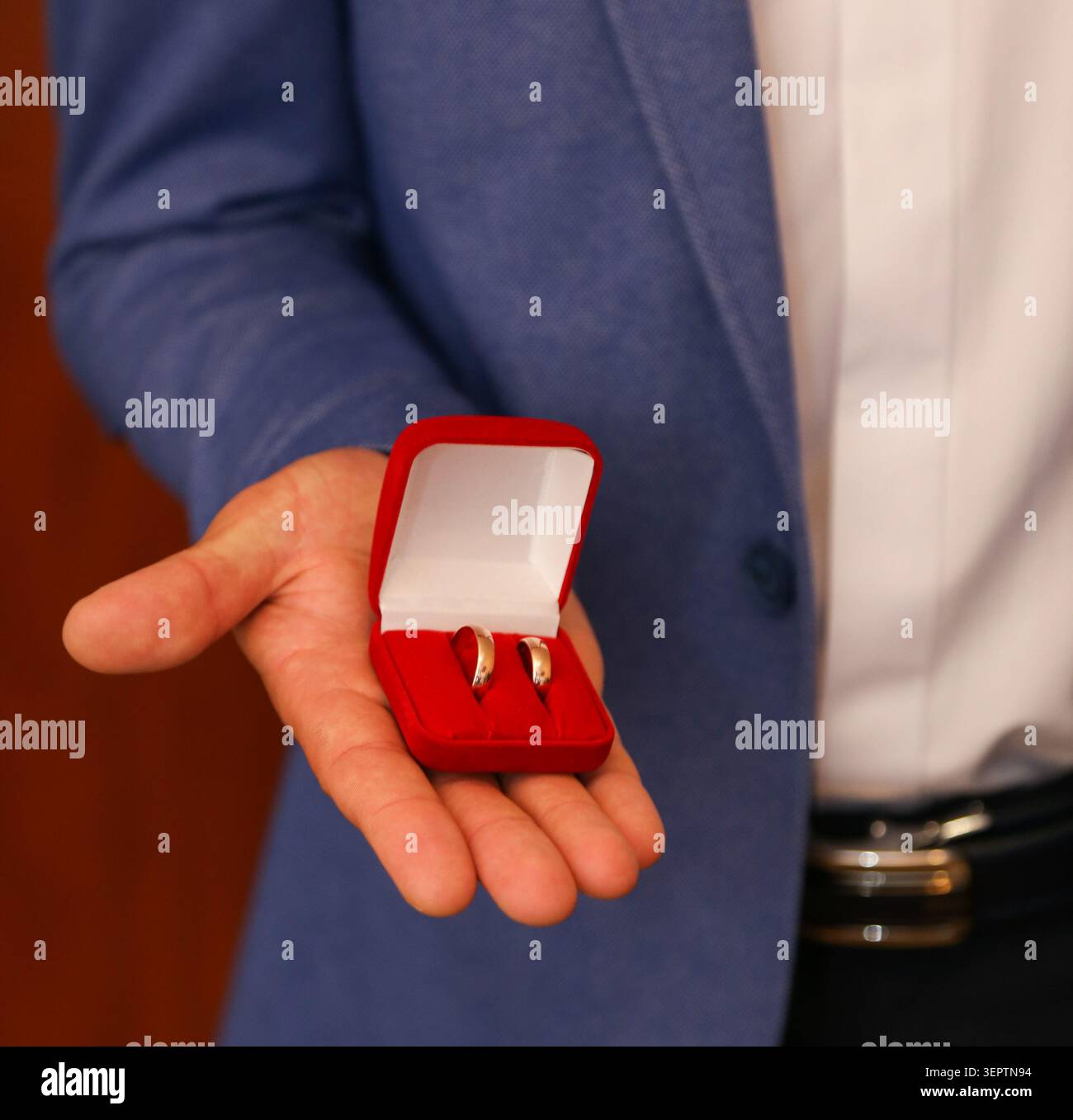 Der Mann trägt einen blauen Blazer, ein weißes Hemd, einen schwarzen Gürtel. Die Finger zeigen vorsichtig Ringe an, um eine Präsentation oder einen Vorschlag vorzuschlagen. Bilder werden intim aufgenommen. Ideal für Stockfoto