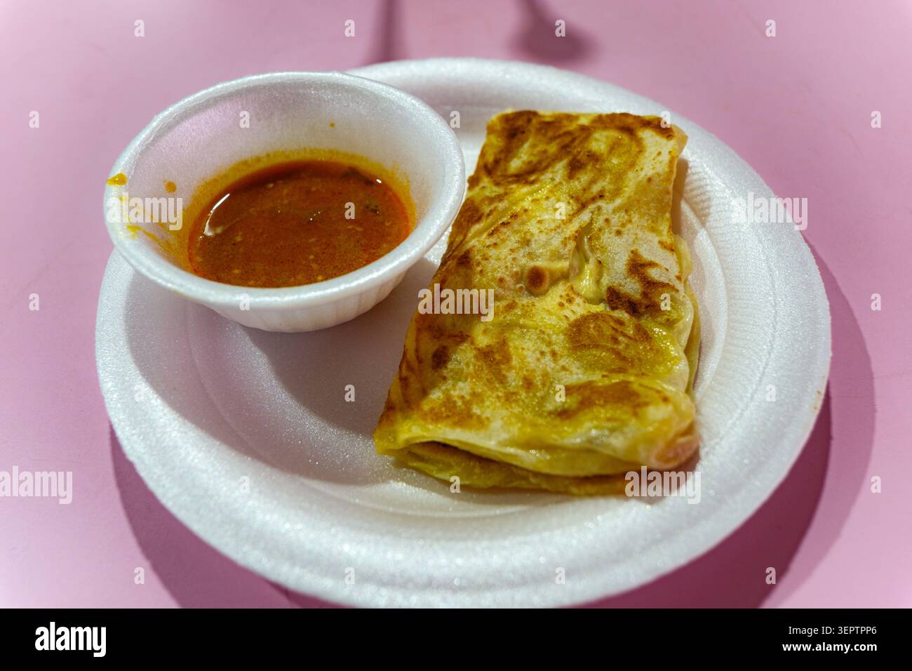 Traditionelles Singapore Roti Prata mit scharfer Curry Dipping Sauce serviert in Little India auf einem weißen Teller mit rosa Hintergrund. Stockfoto