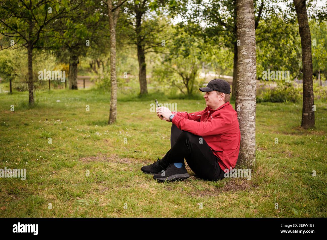Ein Mann, der sich in der Natur entspannt und mit der Technologie seines Mobiltelefons verbunden ist Stockfoto