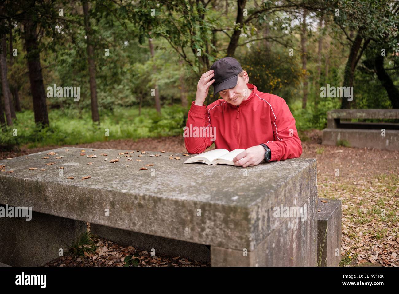 Ein Mann liest ein Buch, während er sich tief an einem Steintisch konzentriert Stockfoto