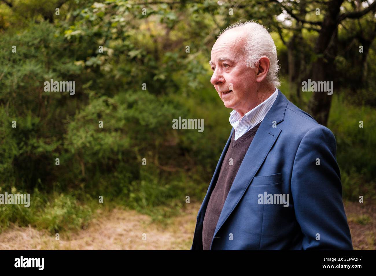 Seniorenmann in einer Anzugsjacke, der draußen im grünen Laub läuft Stockfoto