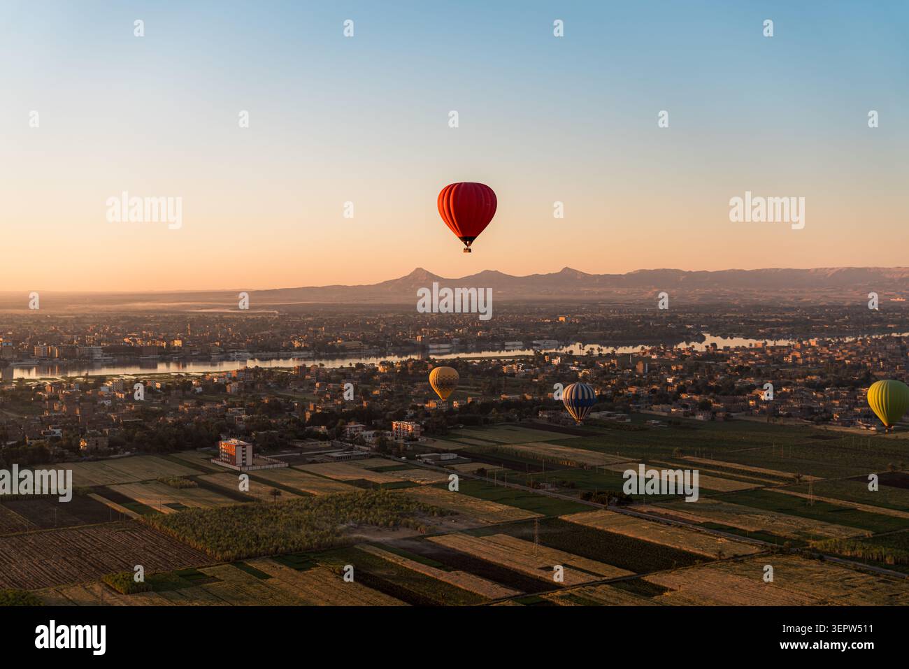 Luftaufnahme der landwirtschaftlichen Landschaft des Niltals nahe Luxor, Ägypten. Ein einzelner Heißluftballon ist in der Ferne über dem grünen Ackerland sichtbar. Blauer Himmel. Stockfoto