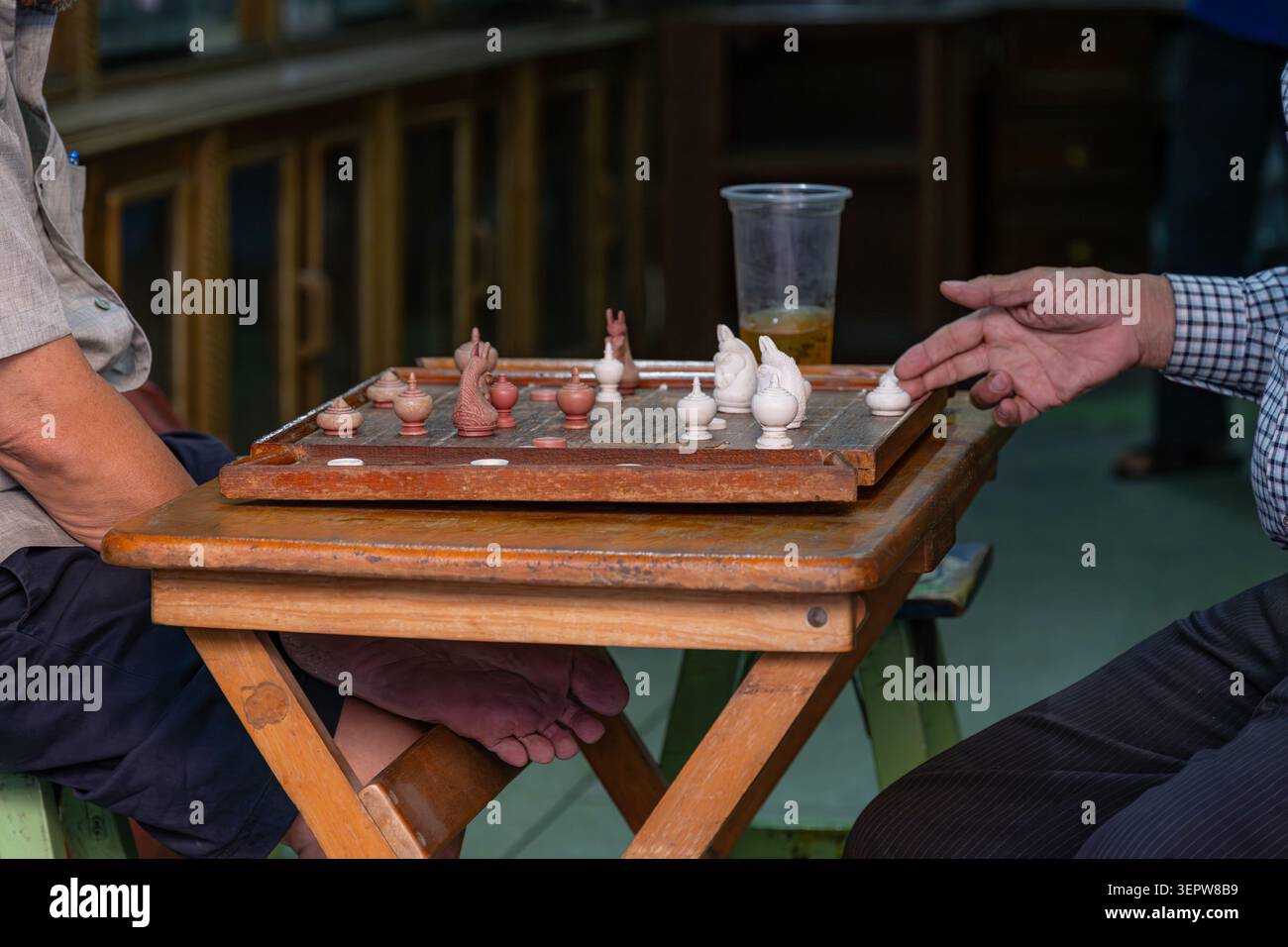 Zwei ältere Männer spielen ein traditionelles thailändisches Schach auf einem rustikalen Holztisch in einer ungezwungenen lokalen Umgebung. Stockfoto