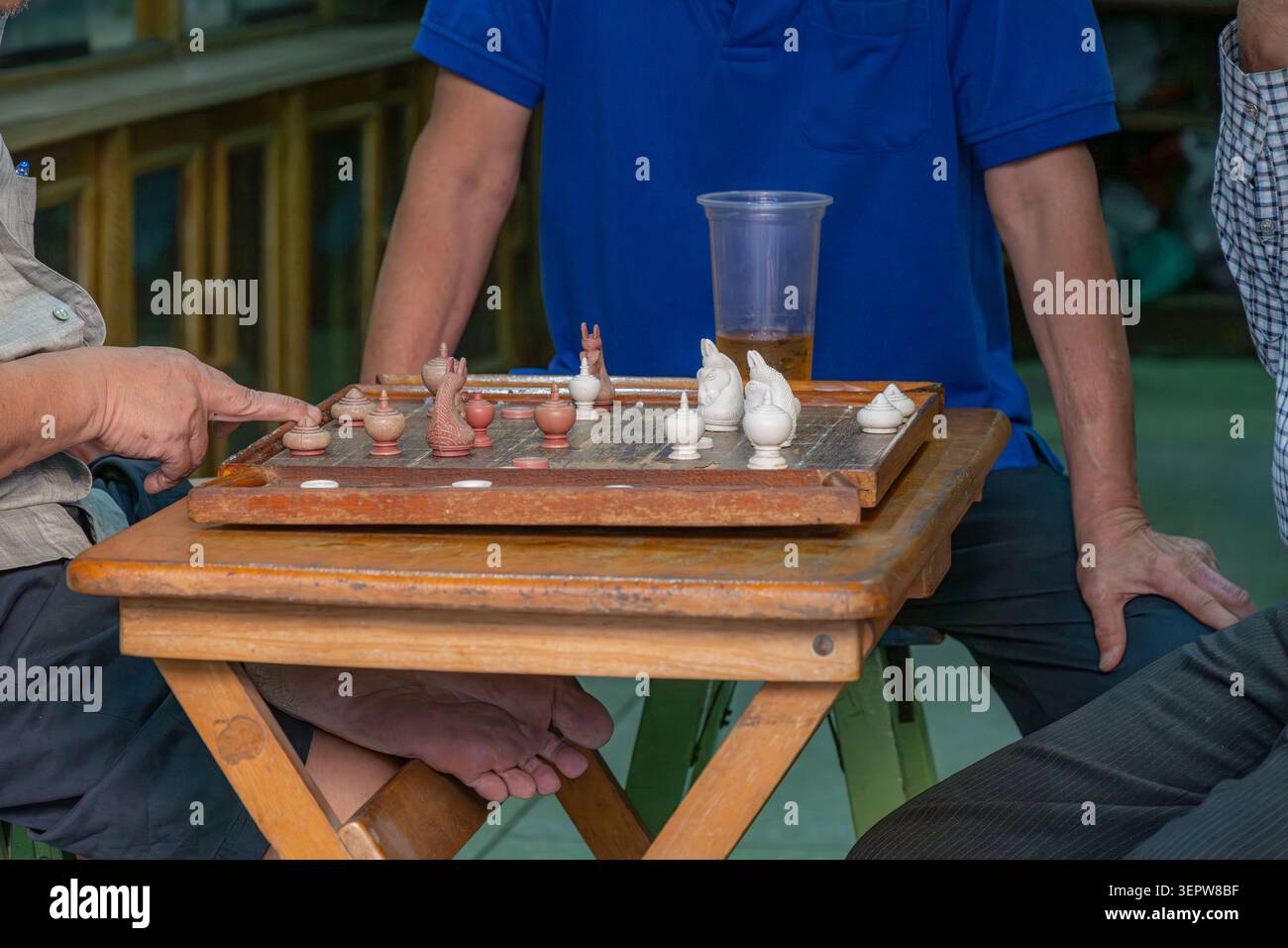 Nahaufnahme von zwei Männern, die in einem durchdachten Spiel Thai-Schach mit Schwerpunkt auf Holzstücken und Brett verwickelt sind. Stockfoto