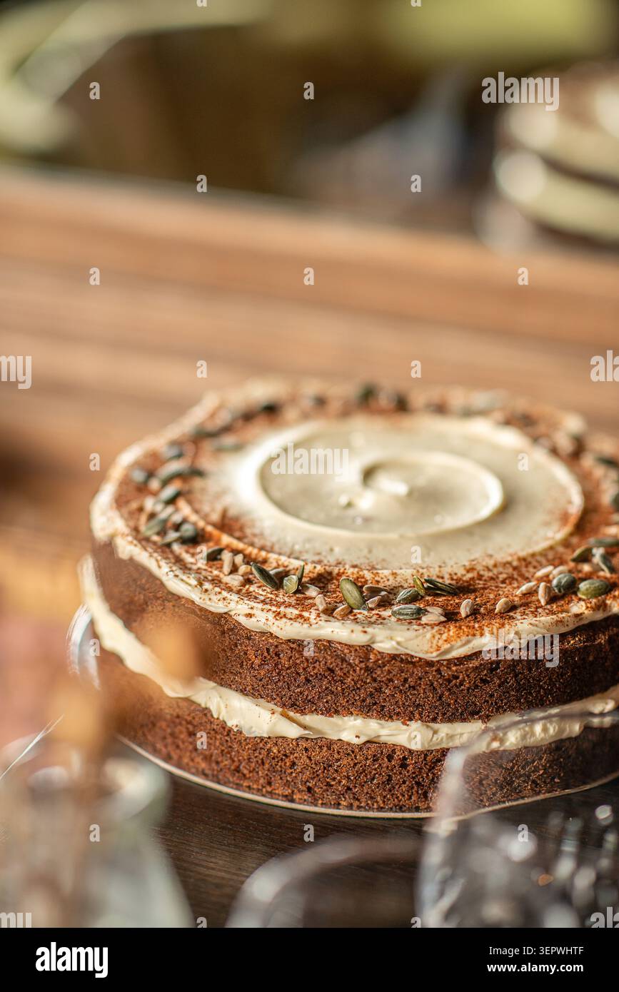 Ein rustikaler, doppelschichtiger Karottenkuchen, gefüllt mit Frischkäse-Frosting, mit Zimt bestäubt und mit Kürbiskernen garniert. Stockfoto