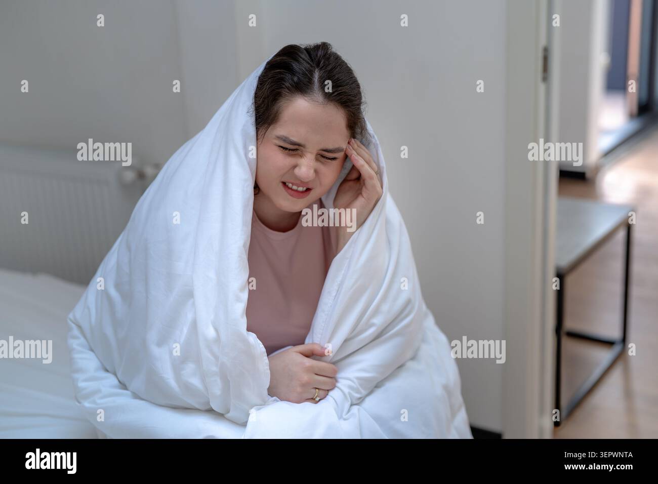 Unwohl Frau, in Decke gewickelt, sitzend auf dem Bett, berührend Schläfen, während sie an schweren Kopfschmerzen litt. Weibliche Grimassen vor Schmerzen und Unwohlsein, Conce Stockfoto