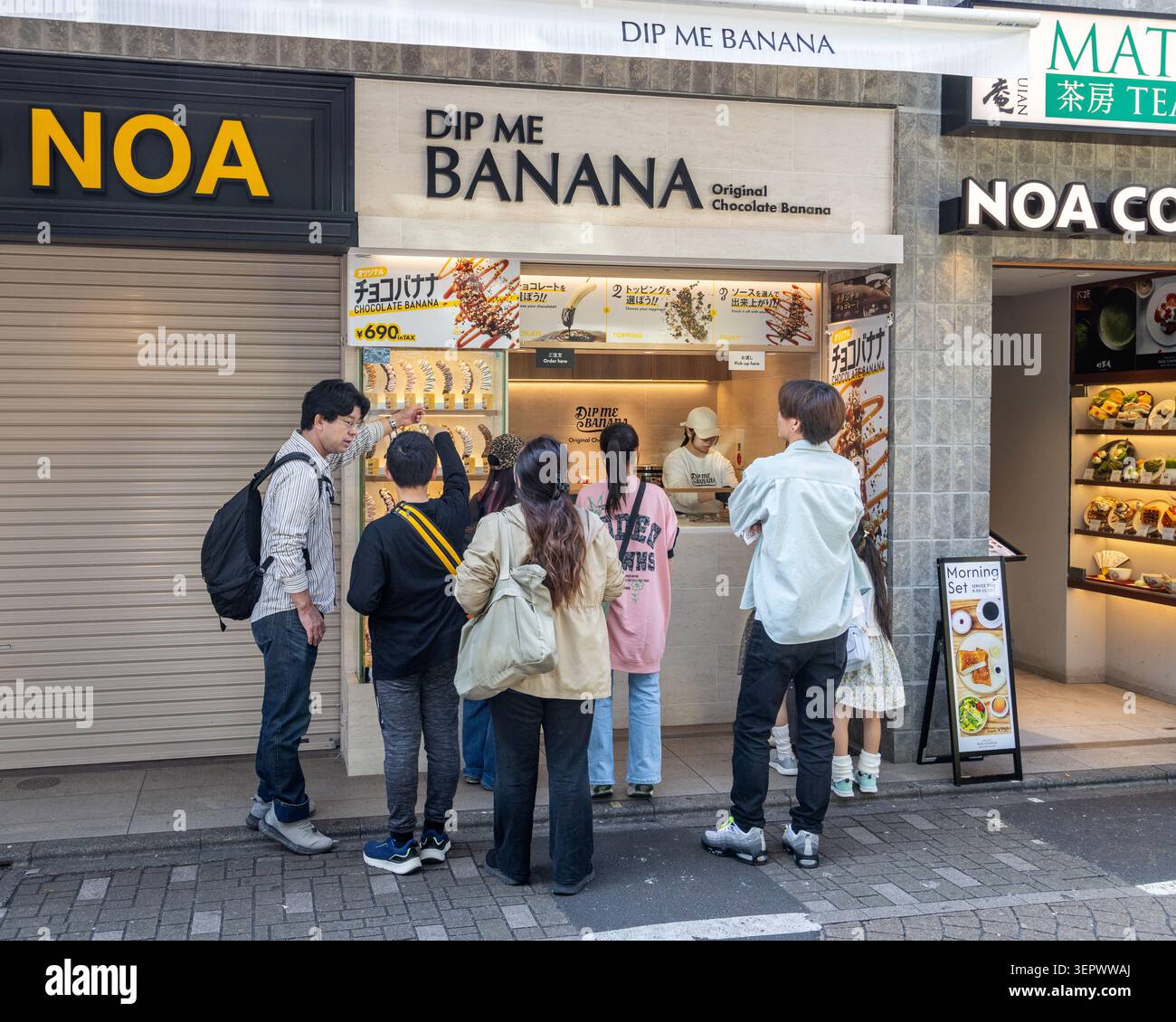 Kunden stehen bei DIP ME BANANA, einem Schokoladen-Bananen-Spezialitätenladen in der Takeshita-Straße in Harajuku, Tokio, Japan, Schlange. Stockfoto