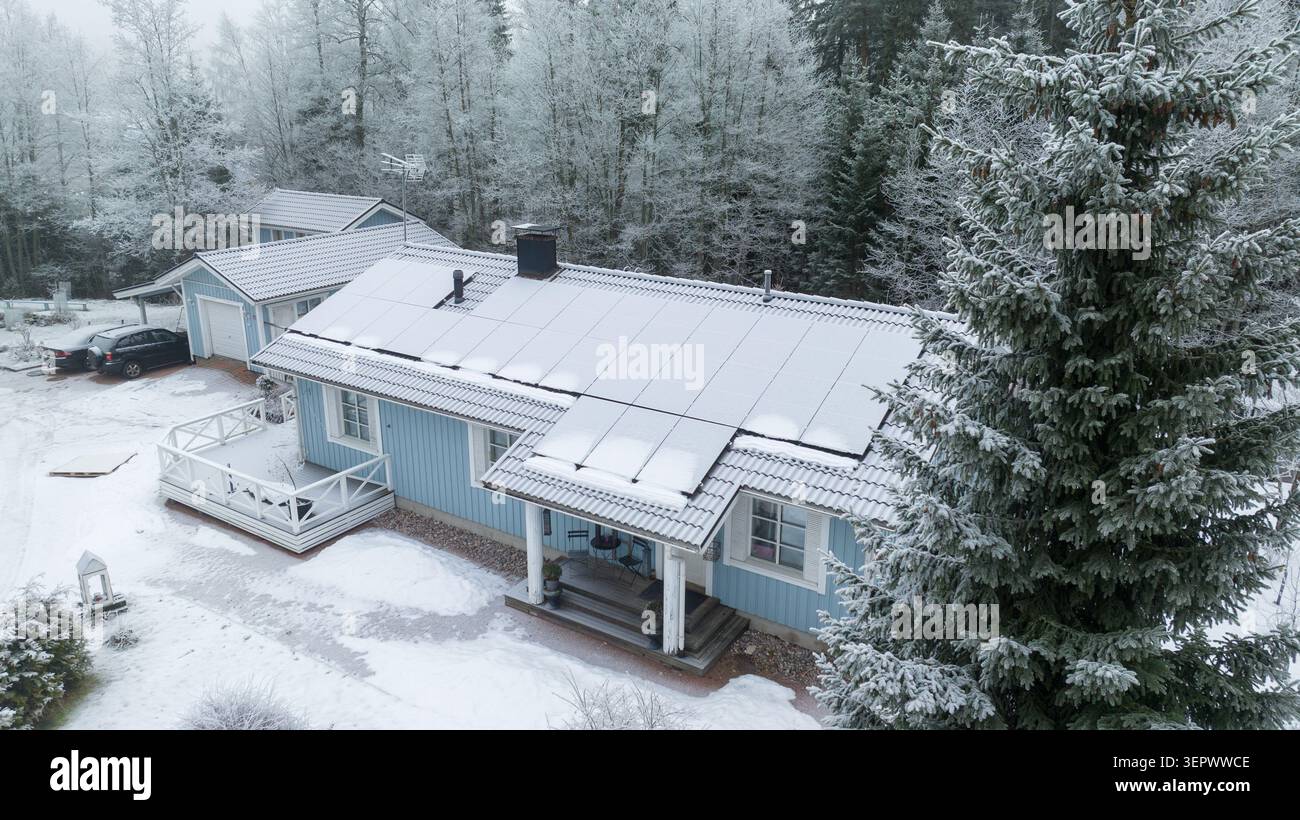 Luftaufnahme eines blauen Holzhauses mit Solarpaneelen auf dem Dach, umgeben von einem frostigen Wald im Winter Uusimaa, Finnland. Stockfoto