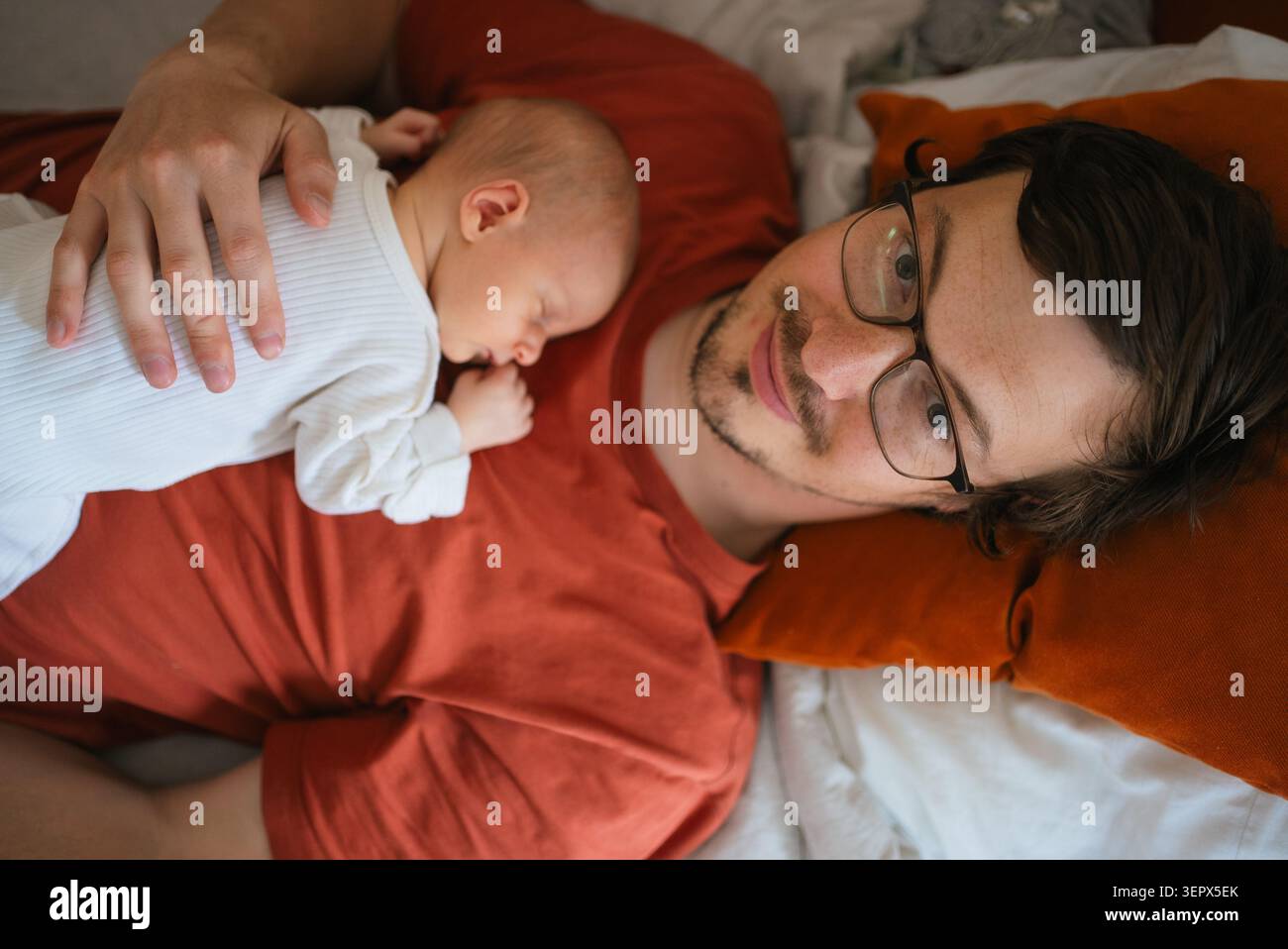Vater und neugeborener Sohn verbinden sich, schlafen zusammen auf einem Bett, erleben neue Vaterschaft und neues Familienleben, genießen elterliche Liebe und intime Momente Stockfoto