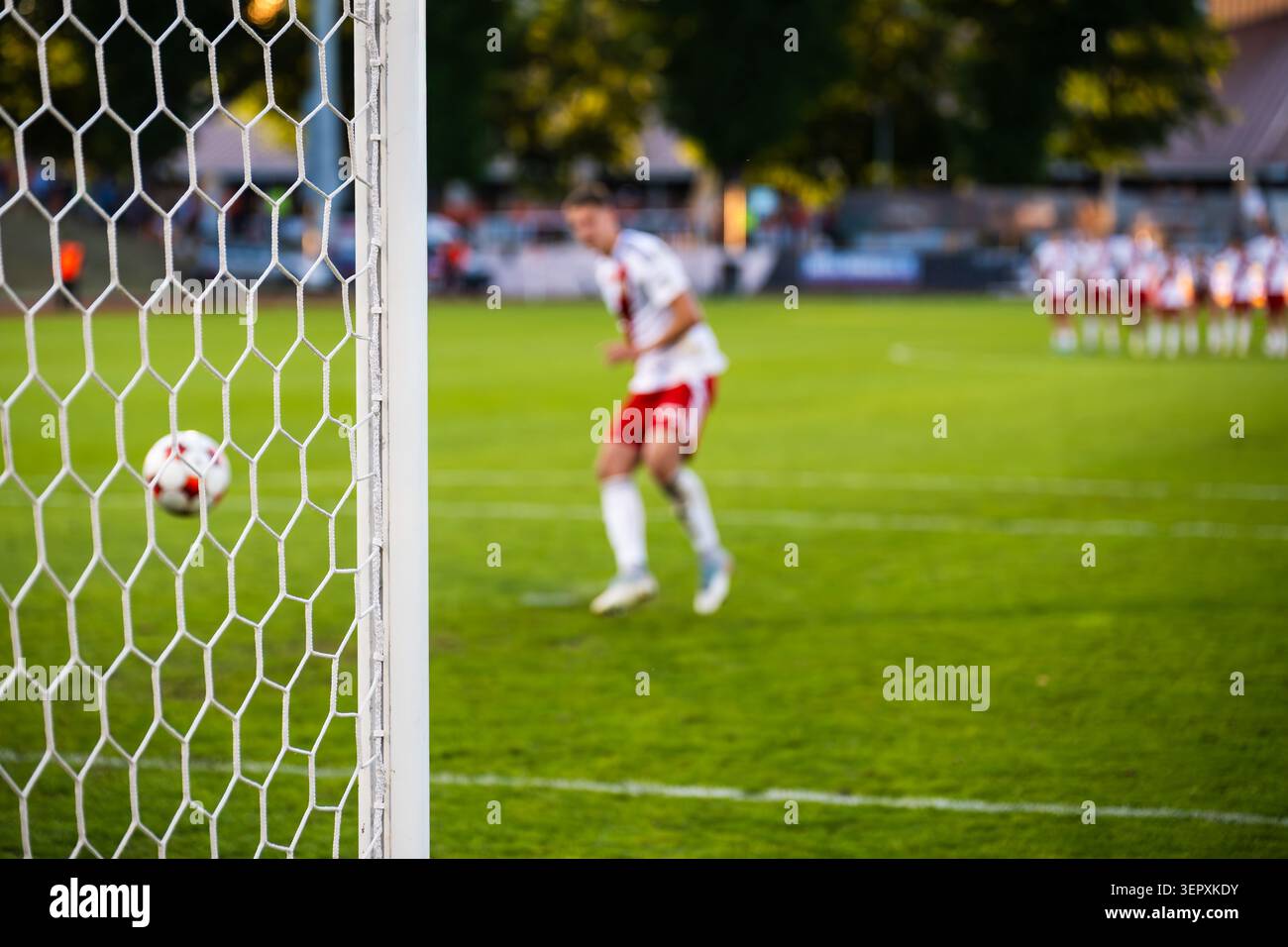 Ein Fußballspieler in weißer Uniform, der während eines Fußballspiels einen Strafschuss in Richtung Tor schießt, gesehen durch das Netz. Stockfoto