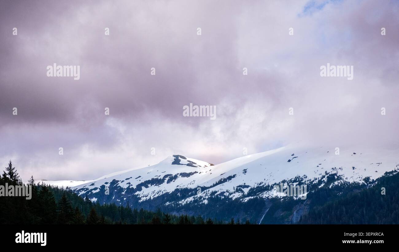 Schnee auf Berggipfeln mit niedrigen Wolken und schattigem Wald Stockfoto