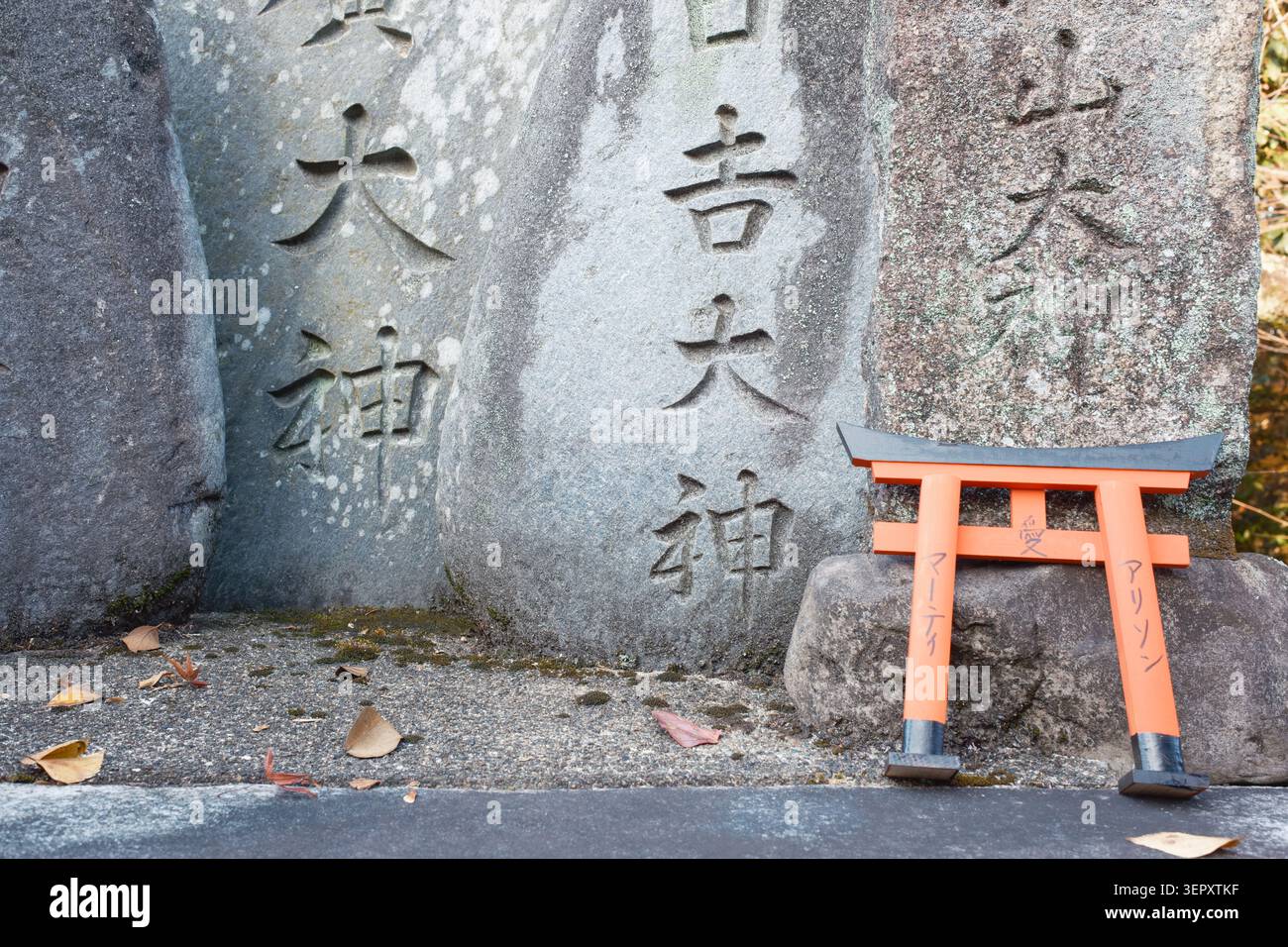 Großes historisches Denkmal aus verwittertem grauem Stein mit geschnitzten vertikalen Inschriften neben einem kleinen orangen hölzernen Torii-Tor, Kyoto, Japan Stockfoto