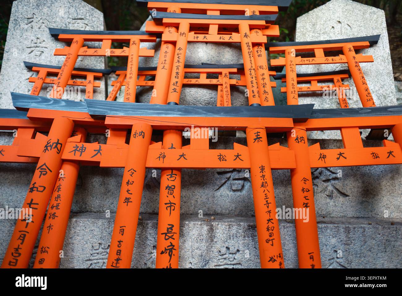 Gruppe von mehreren Miniaturhölzern mit orangefarbenen Torii-Toren mit schwarzen Spitzen, die als Opfergabe an einem schintoistischen Schrein in Kyoto, Japan, gestapelt sind Stockfoto