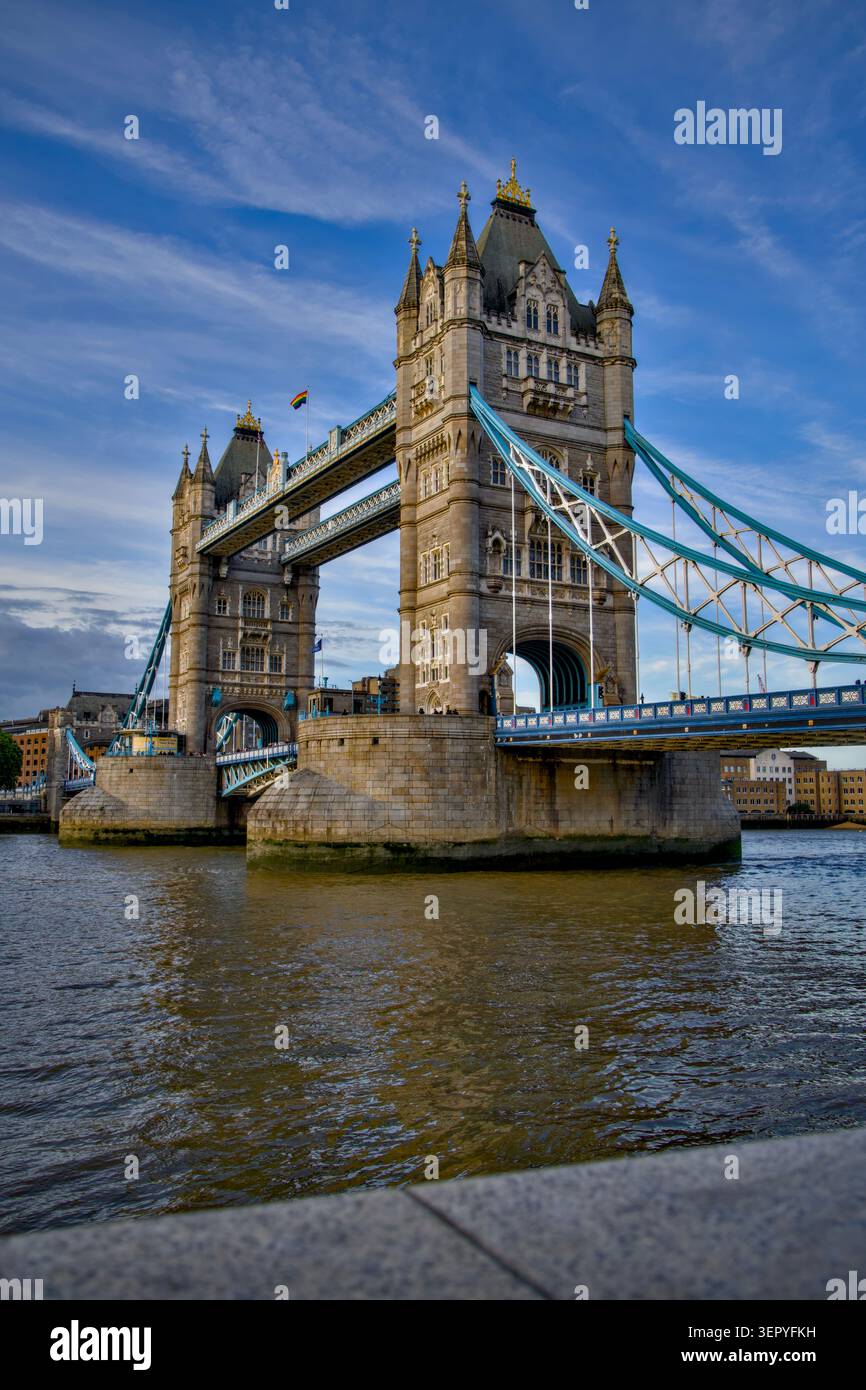 Flacher Blick auf die Tower Bridge in London über die Themse, aufgenommen an einem klaren Tag mit blauem Himmel und verstreuten Wolken. Stockfoto