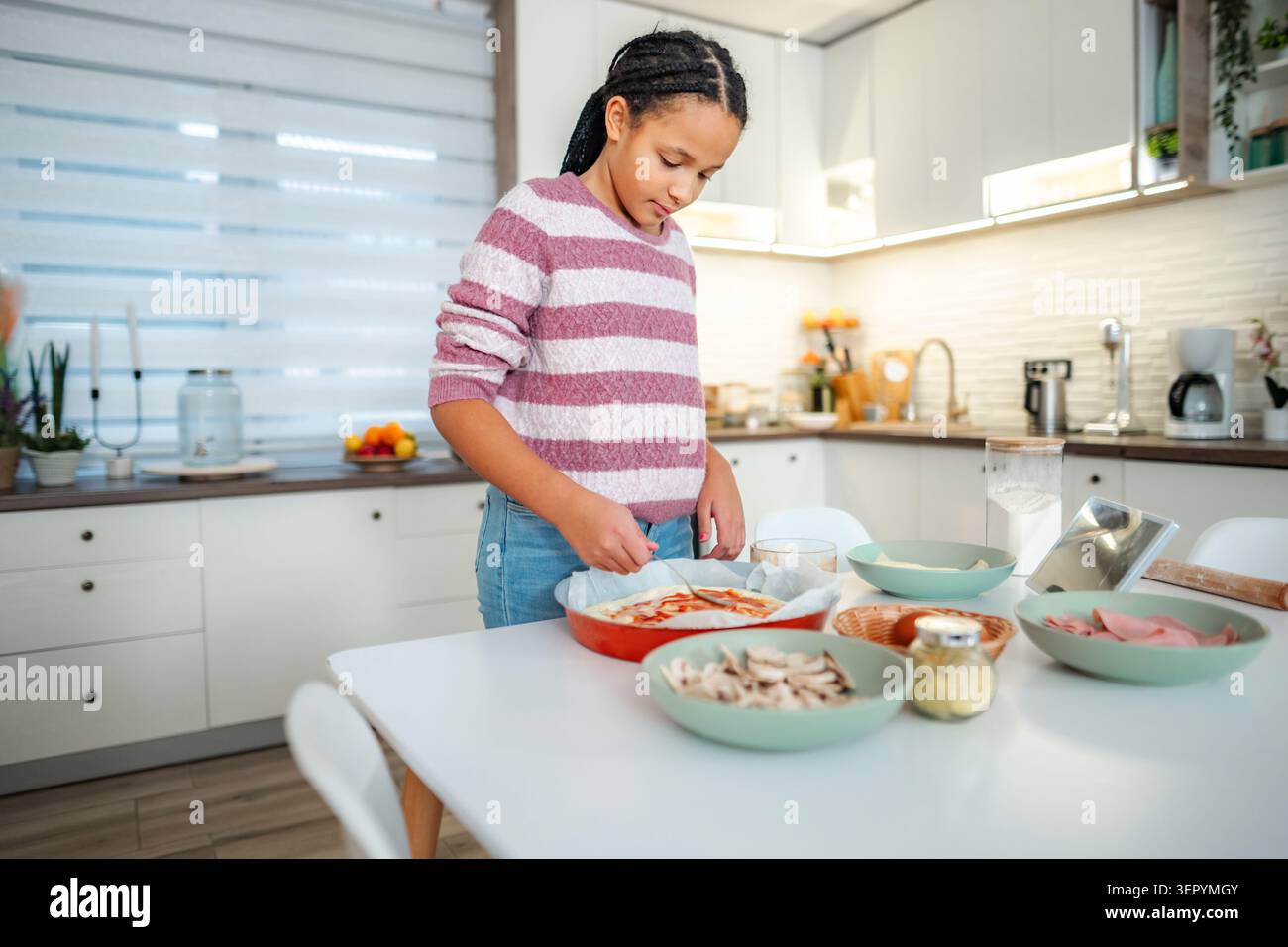 Mädchen, das in der Küche hausgemachte Pizza mit frischen Zutaten zubereitet Stockfoto