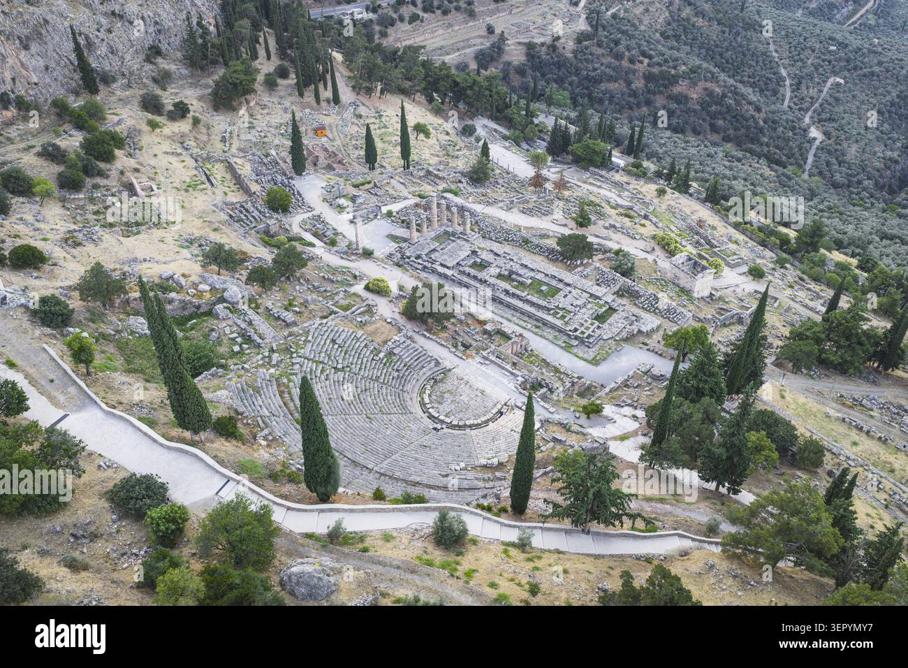 Blick aus der Vogelperspektive auf das antike Theater und den Tempel des Apollo, umgeben von Zypressen und felsigen Hängen in Delphi, Griechenland. Stockfoto