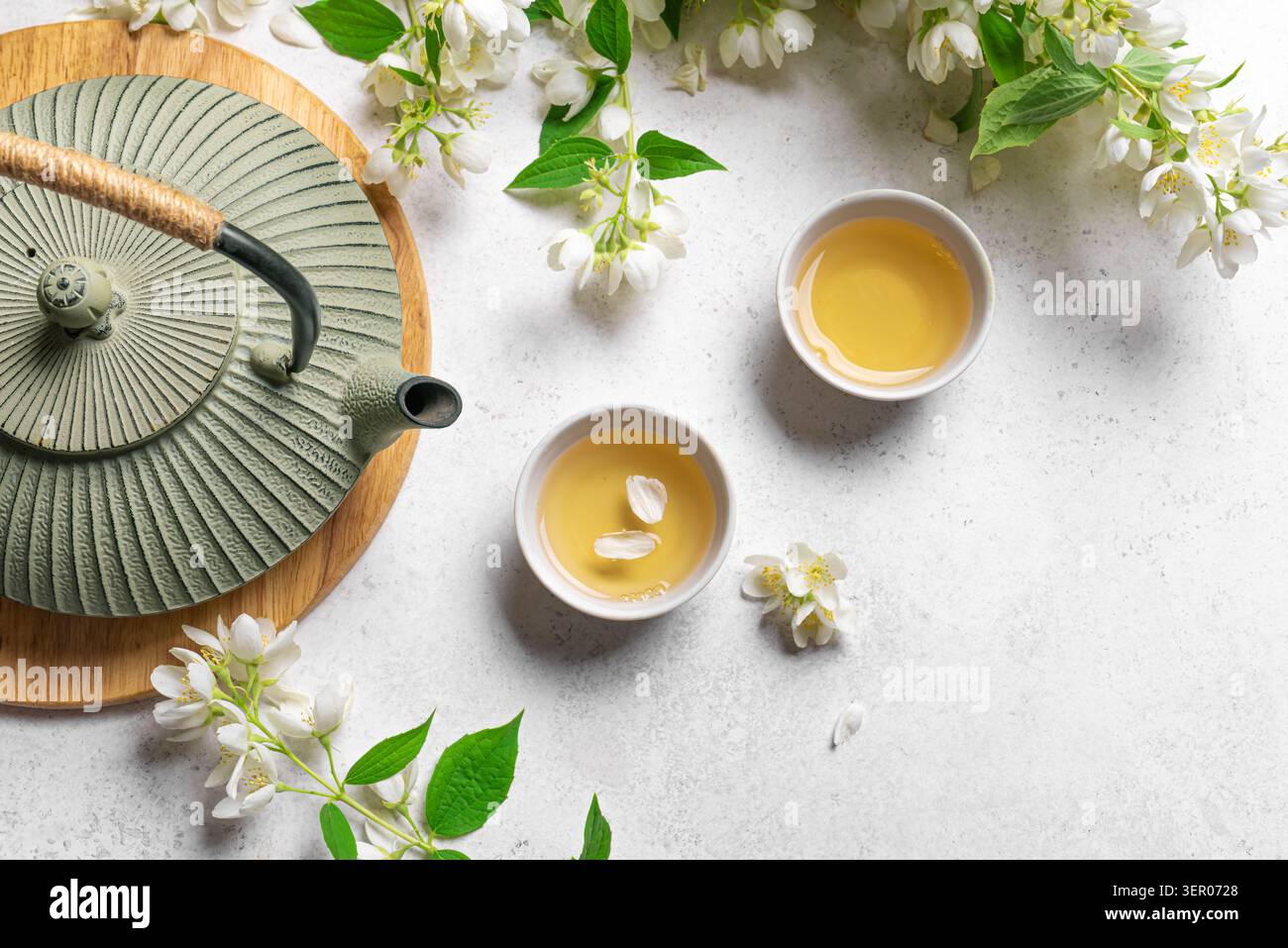 Japanischer grüner Tee mit Jasmin in gusseiserner Teekanne und Teetassen auf weißem Hintergrund, Draufsicht, Kopierraum. Natürlicher Jasmintee und blühende Zweige. Stockfoto