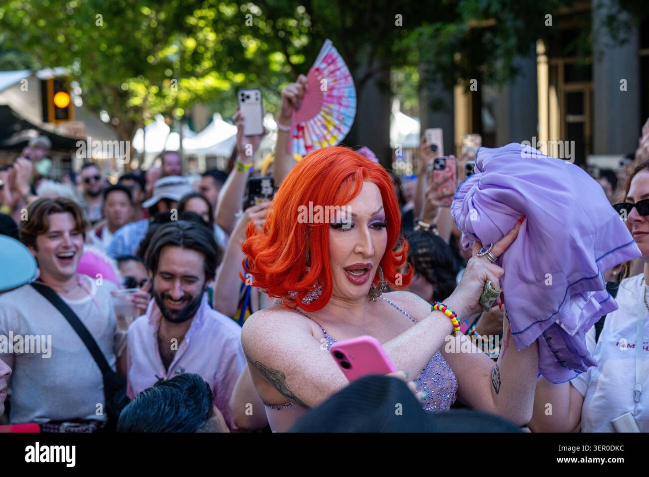 Drag Queen Detox kümmert sich um einen violetten Outfit-Wechsel über ihren orangen Haaren vor einer jubelnden Menschenmenge beim Sacramento Pride Festival. Stockfoto