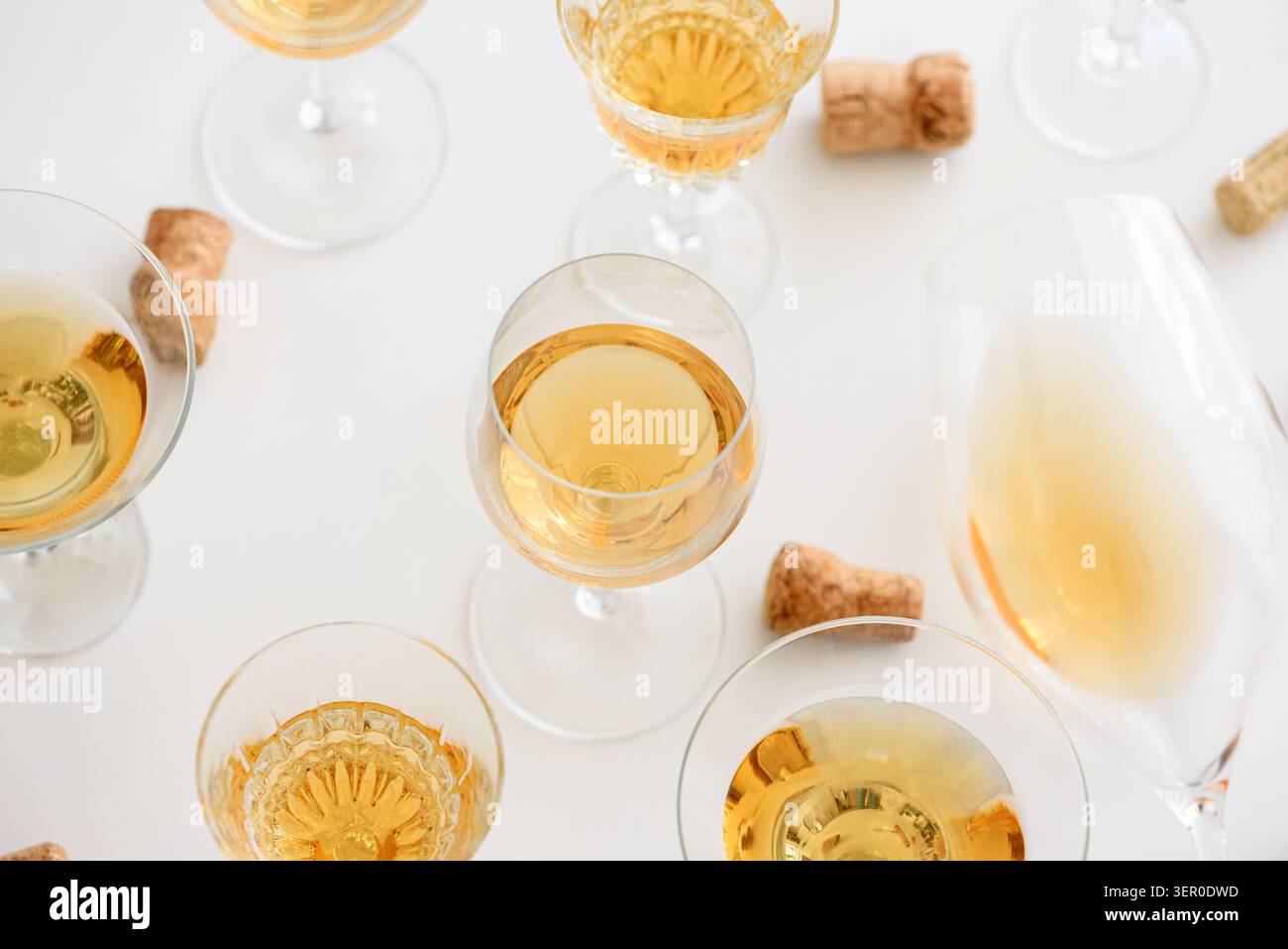 Weißweingläser mit goldener Flüssigkeit und verstreuten Korken sind auf einem hellen Hintergrund angeordnet und symbolisieren Feierlichkeiten, Luxus und festliche Zusammenkünfte Stockfoto