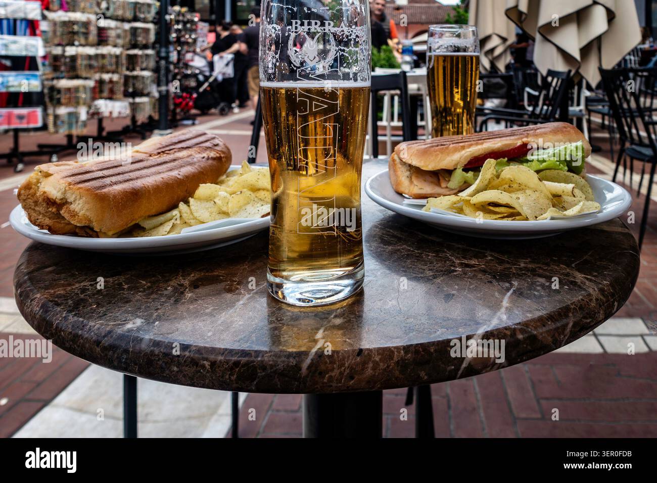 Zwei Pints Birra Korca und zwei Panini-Sandwiches serviert mit Kartoffelchips auf einem Marmortisch in einem Café im Freien in Tirana, Albanien. Stockfoto