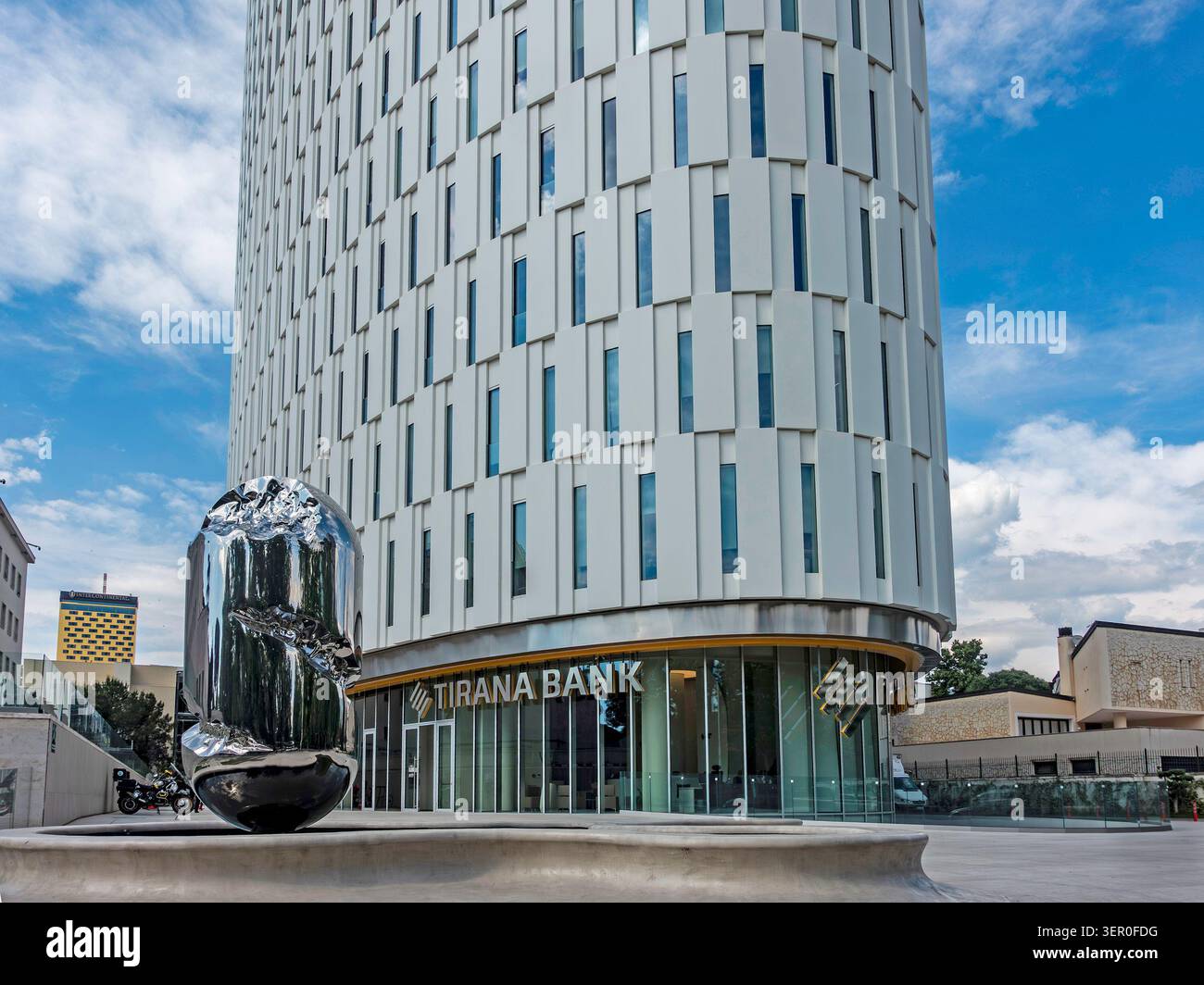 Eine glänzende Metallskulptur in einem Brunnen vor dem modernen Hochhaus der Tirana Bank unter blauem Himmel in Tirana, Albanien. Stockfoto