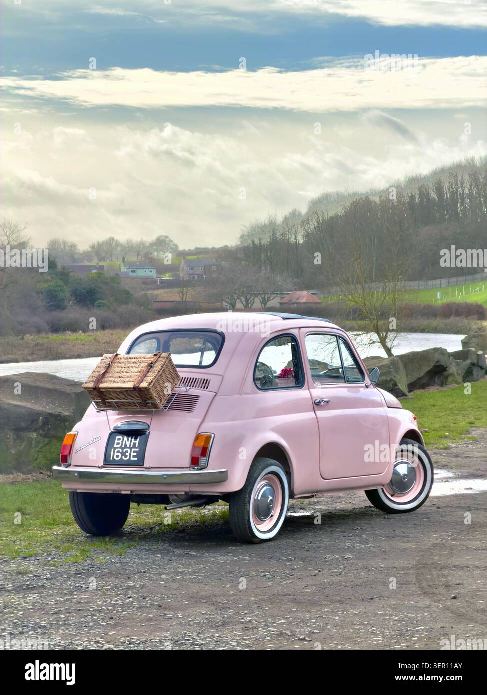 Rosa Fiat 500 Oldtimer, geparkt am Fluss in der Landschaft des vereinigten Königreichs mit Picknickkorb und Gepäckablage hinten Stockfoto