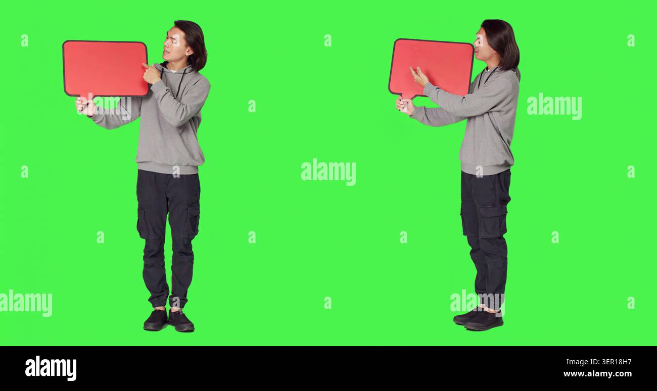 Das männliche Modell posiert mit einer Sprechblase und präsentiert leere Pappe mit Kopierraum vor dem Ganzkörper-grünen Bildschirm, asiatische Person hält rote Pappe für Marketingwerbung. Stockfoto