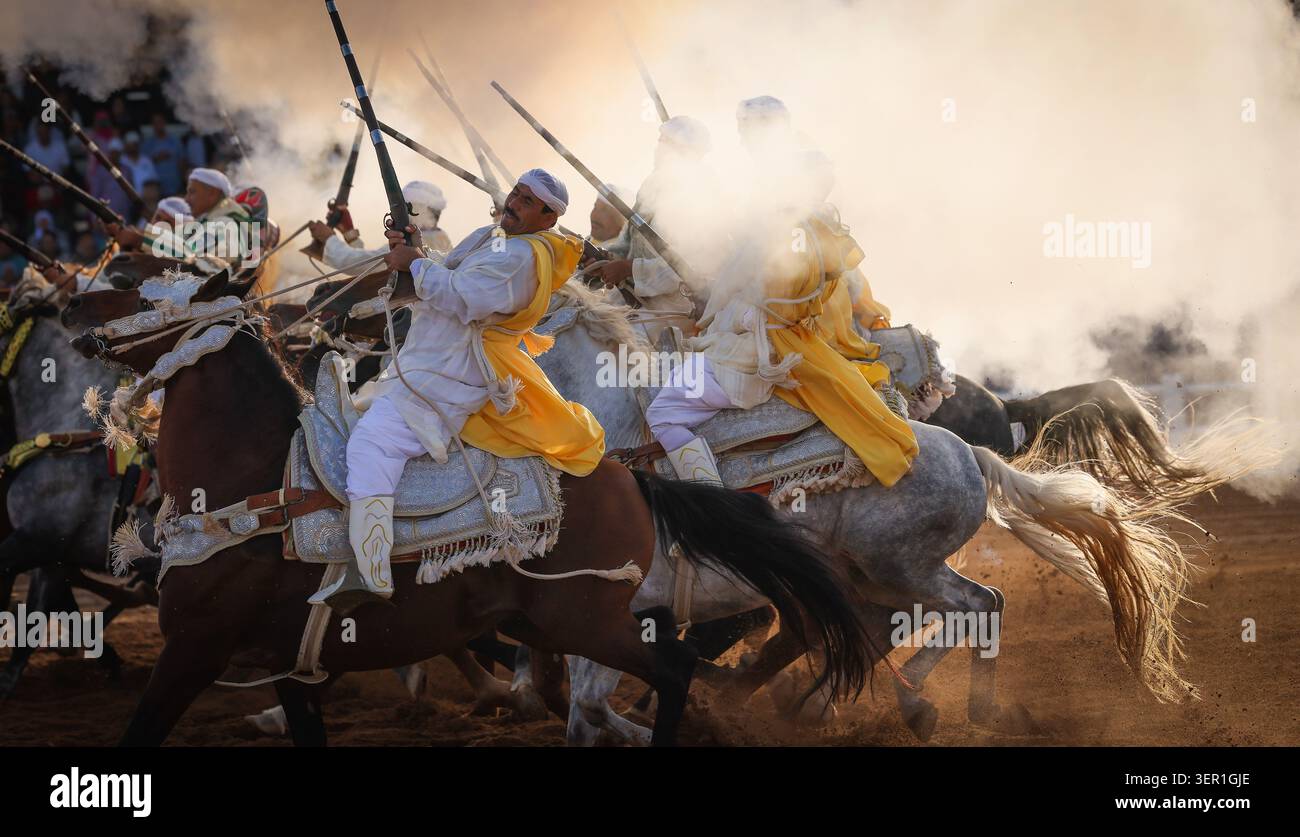 Tbourida, Eine dramatische Szene marokkanischer Fantasien, entfaltet sich, während Reiter durch Staub und Rauch galoppieren und Kraft, Eleganz und Tradition vermischen. Marokko Stockfoto