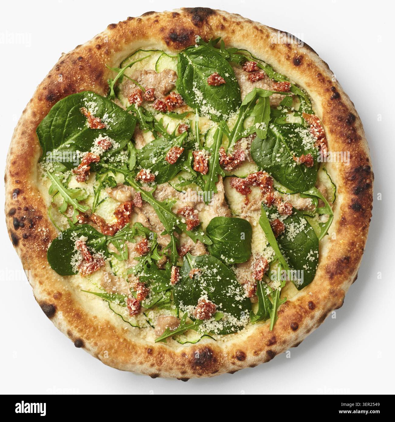 Blick von oben auf eine vegetarische Pizza mit Zucchini, Spinat, sonnengetrockneten Tomaten und Parmesankäse mit appetitlichen Zutaten Stockfoto