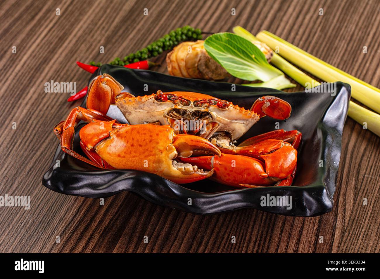 Frisch gedämpfte Krabben, serviert mit Zitronengras, Galgant, Kaffir-Limettenblättern und roten Chilis auf einem dunklen Teller mit leuchtender Orangenschale und Aroma Stockfoto