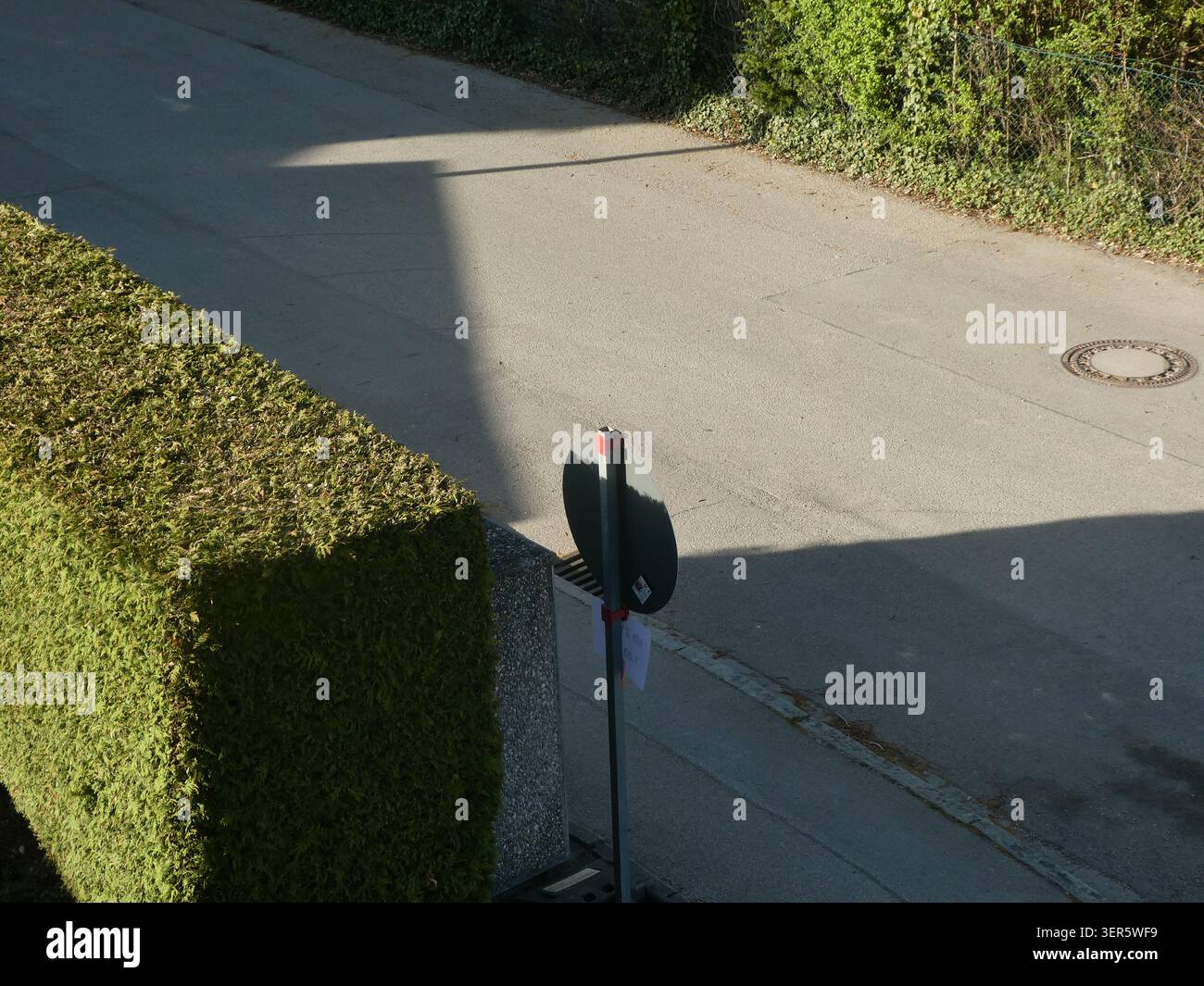 Optische Illusion: Das Straßenschild ist nicht gebrochen, aber der grüne Heckenschatten verschmilzt seinen oberen Teil mit der Farbe der Straße Stockfoto