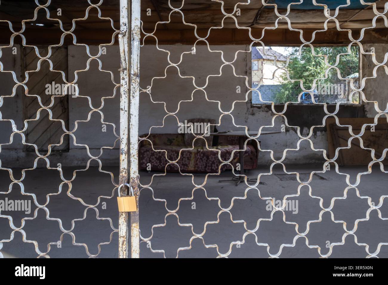 View through a decorative metal security grill into a cozy semi-outdoor Asian veranda (sit-out) with sofa and table. Typical South Asian residential a Stockfoto