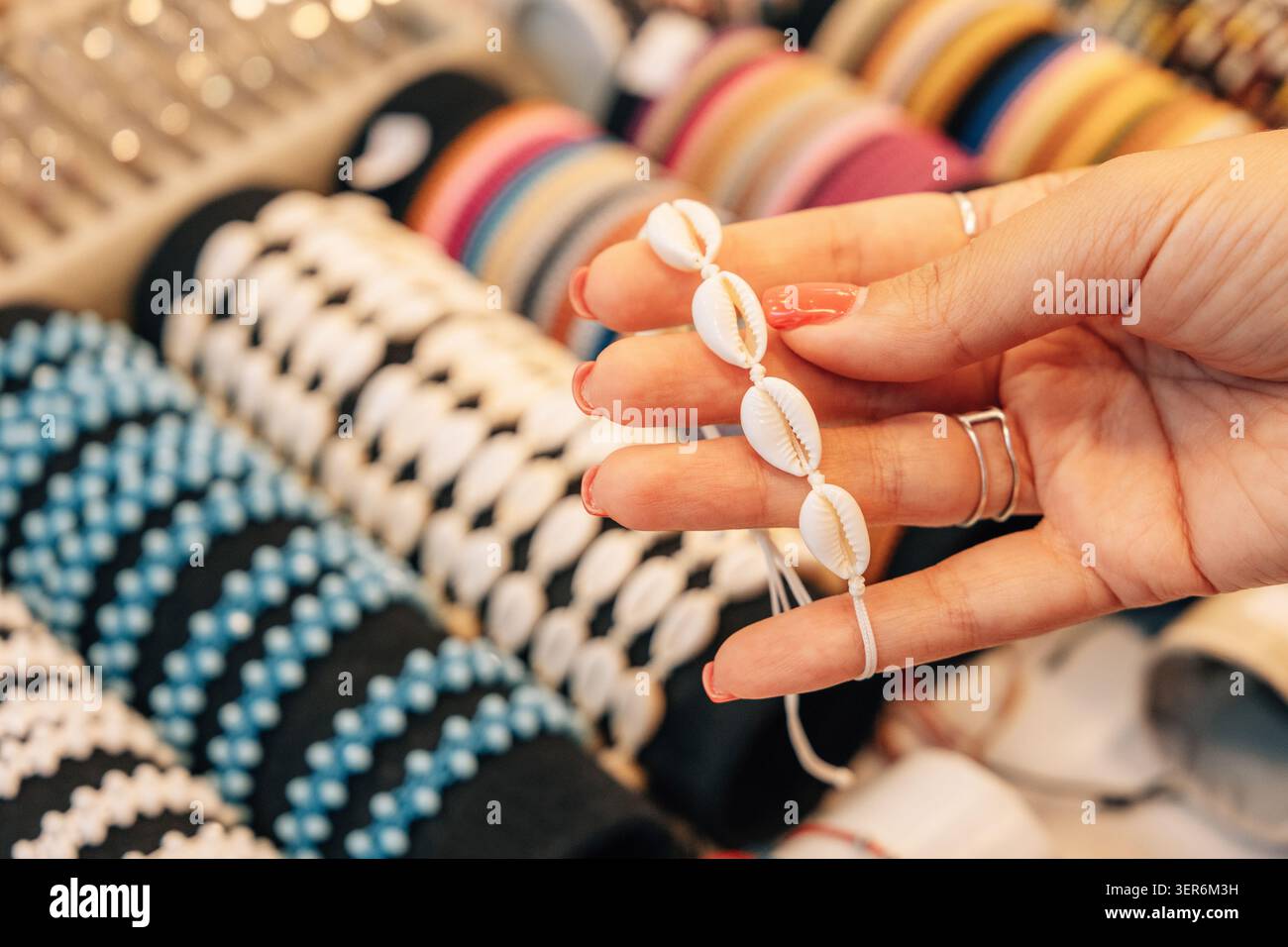 Nahaufnahme einer Hand, die ein handgefertigtes Kaurimuschelarmband hält, und entdecken Sie modische Accessoires in einer lebendigen Ladenpräsentation Stockfoto