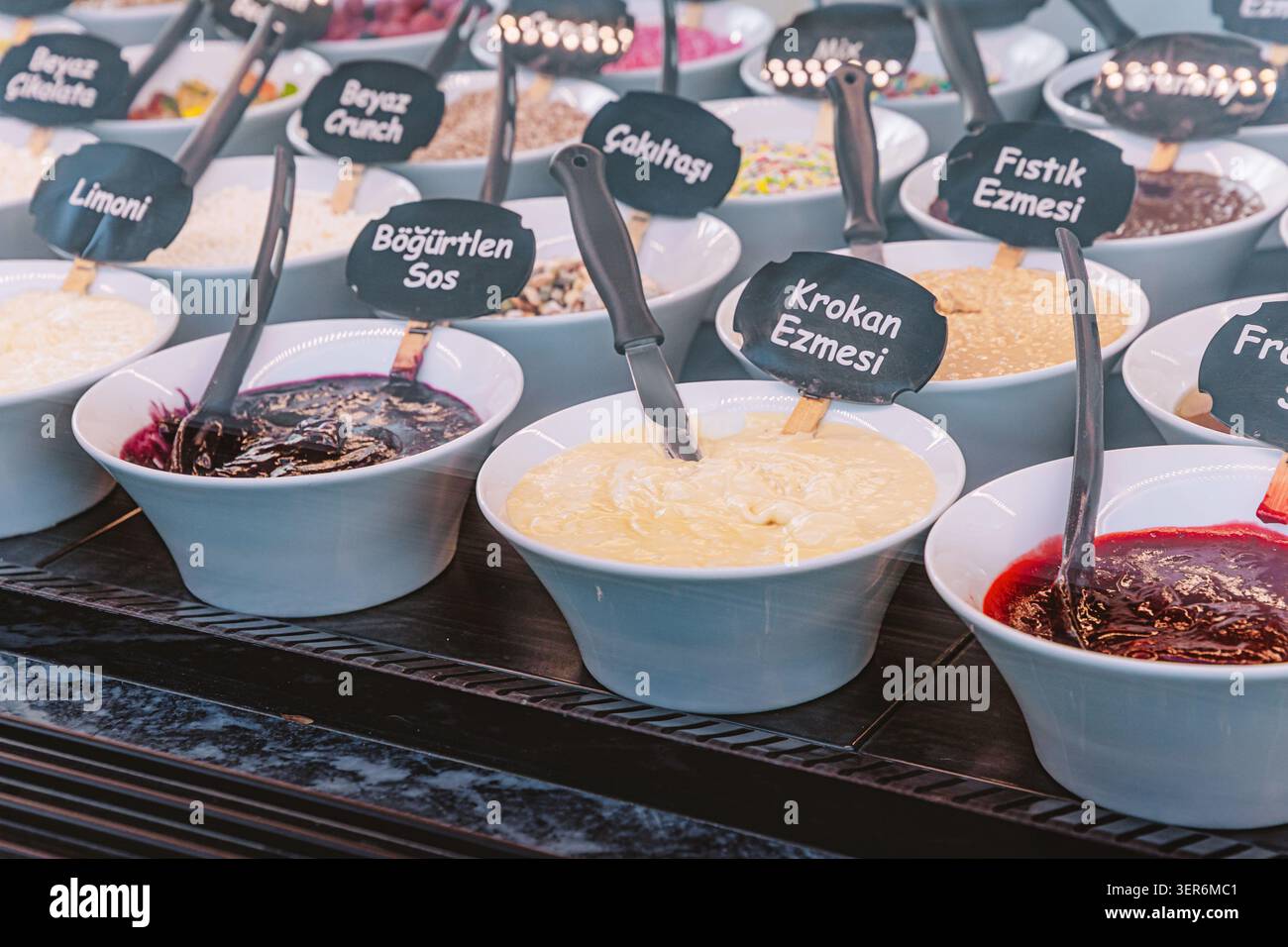 Schüsseln mit vielen verschiedenen süßen Dessertgarnituren, Saucen und Aufstrichen werden an einer Eis- oder Waffelbar ausgestellt Stockfoto