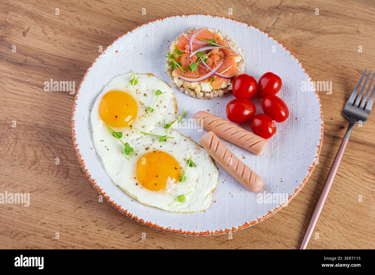 Spiegeleier mit Wurst, Kirschtomaten und Buchweizenbrot mit Lachsfisch Stockfoto