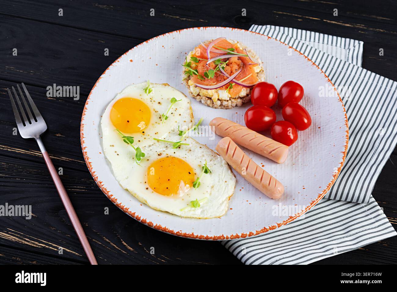 Spiegeleier mit Wurst, Kirschtomaten und Buchweizenbrot mit Lachsfisch Stockfoto