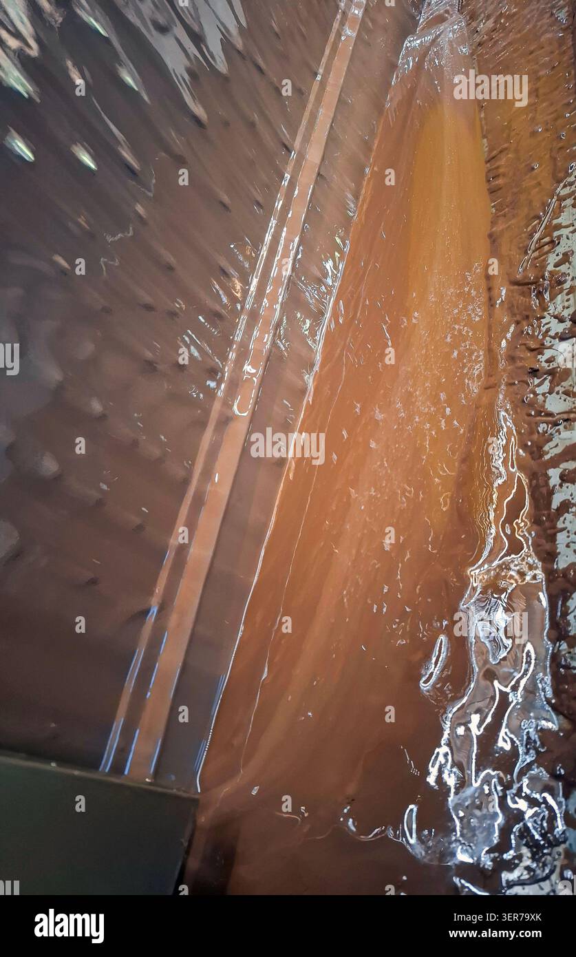 Reichhaltige geschmolzene Milchschokolade fließt während eines professionellen Temperierprozesses in einer Süßwarenfabrik sanft. Die glänzende Oberfläche zeigt die Vorsicht Stockfoto