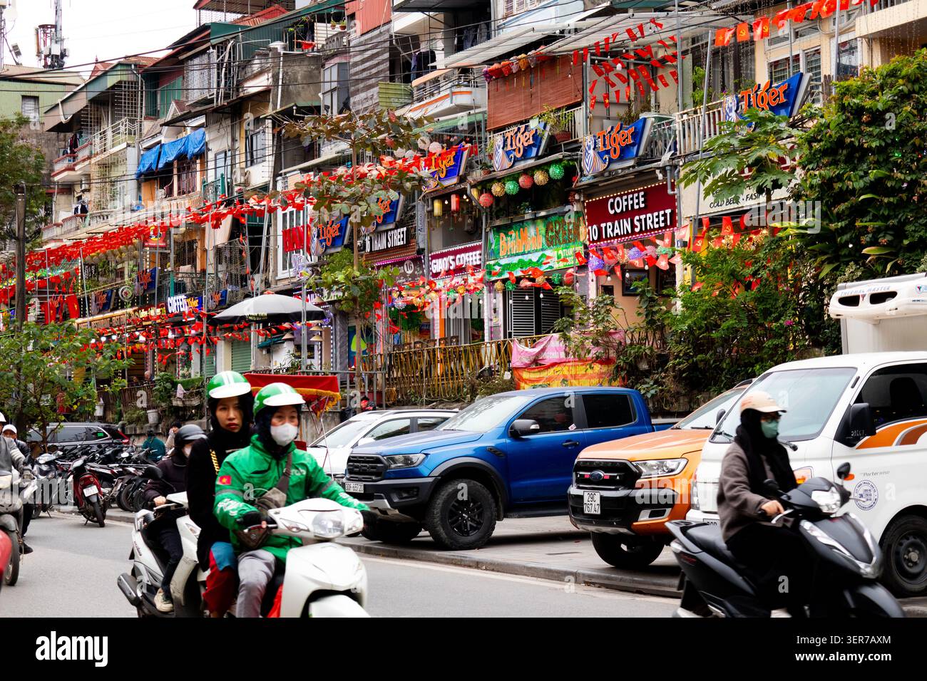 Straßenblick mit Fahrzeugen hohe Gebäude, die zurück auf die berühmte Bahnstraße mit Werbung bewerten Kaffee und Tiger Bier Hanoi Vietnam Stockfoto