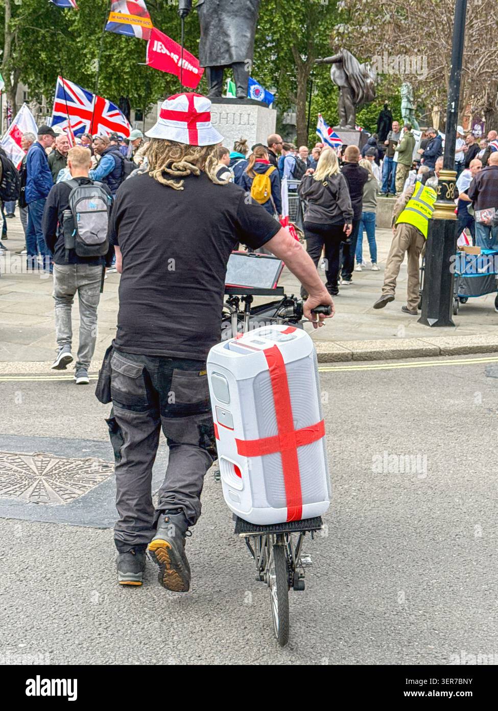 London, England, Großbritannien - 16. Mai 2026: Person mit einem St. George England Hut, der ein Fahrrad mit einem Soundsystem in den Farben der St. George Flagge schiebt Stockfoto
