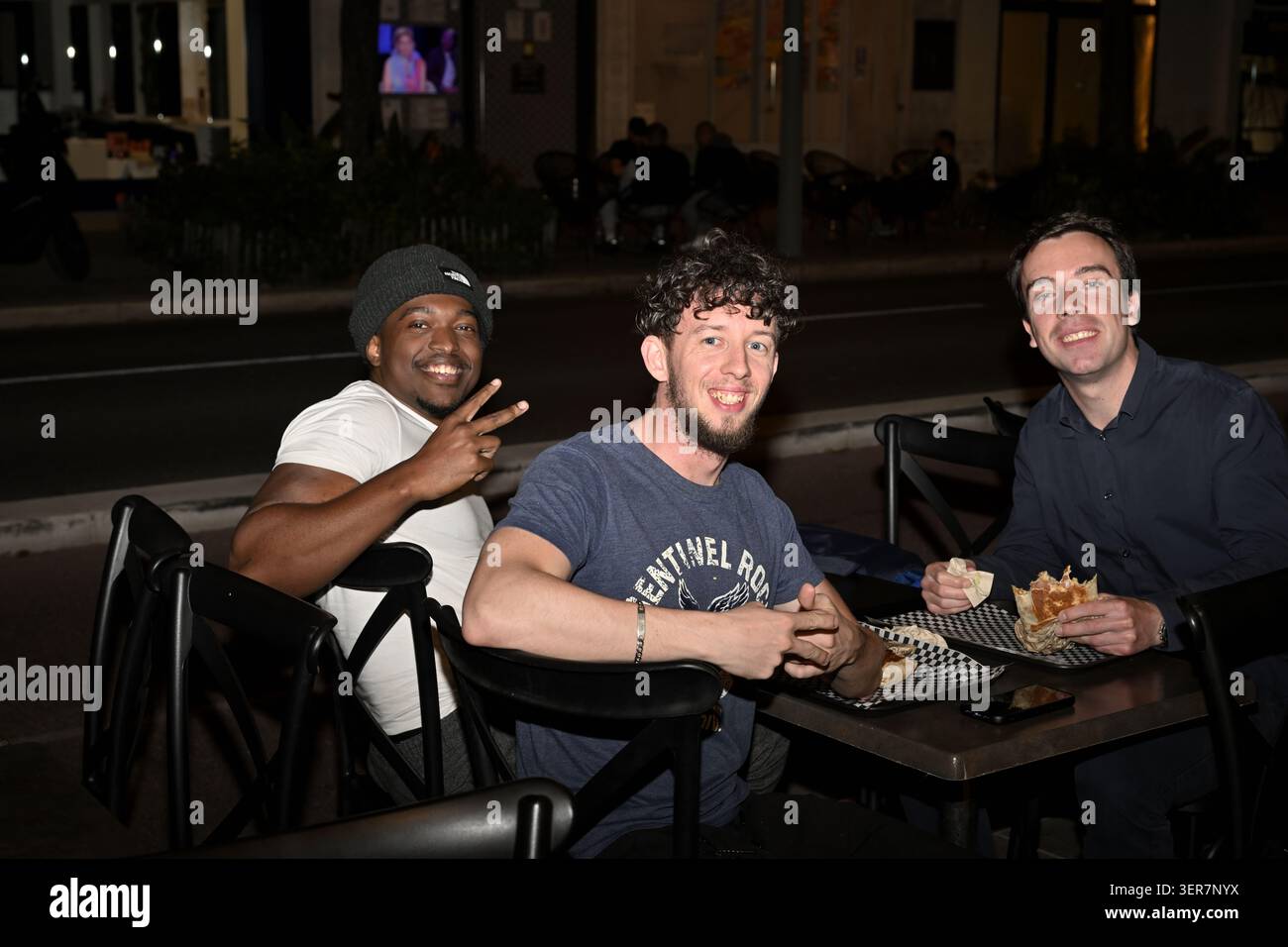 Drei glückliche Jungs am Abend sitzen am Tisch des Restaurants und essen Fast Food Stockfoto