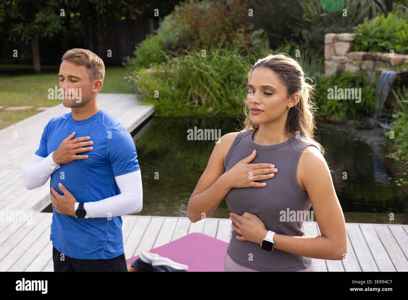Verschiedene Freunde, die an Deck am Teich atmen, fallen in Aktivkleidung mit Uhren und lila Matte Stockfoto
