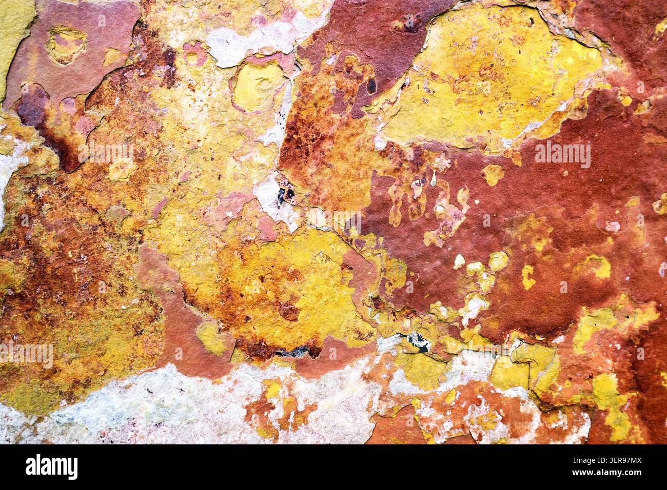 Nahaufnahme einer farbenfrohen, strukturierten Felsoberfläche mit natürlichen Rot- und Gelbtönen, die einem abstrakten Gemälde ähneln. Diese lebendige Mineralienpräsentation Stockfoto