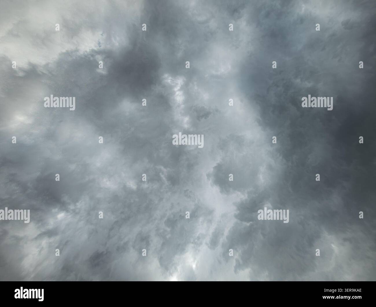 Die Tiefwinkelansicht erfasst turbulenten Himmel voller dunkler Sturmwolken. Licht bricht durch und erzeugt eine unheilvolle Atmosphäre des bevorstehenden Wetters. Stockfoto