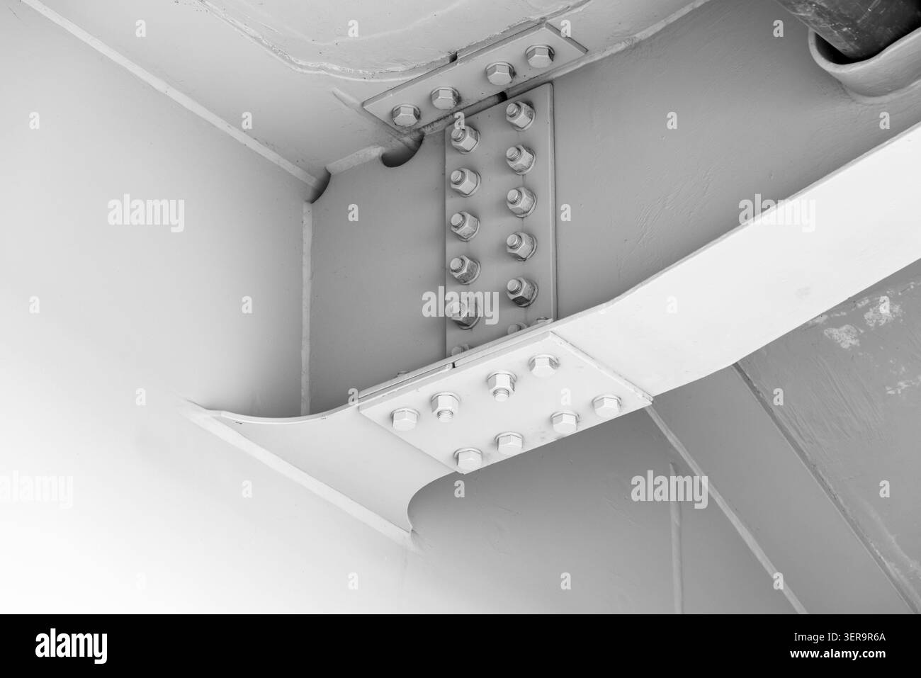 Nahaufnahme einer lackierten Stahlträgerverbindung, die Schrauben, Platten und Schweißnähte in einer industriellen Strukturverbindung unter einer Brücke zeigt und den Motor betont Stockfoto