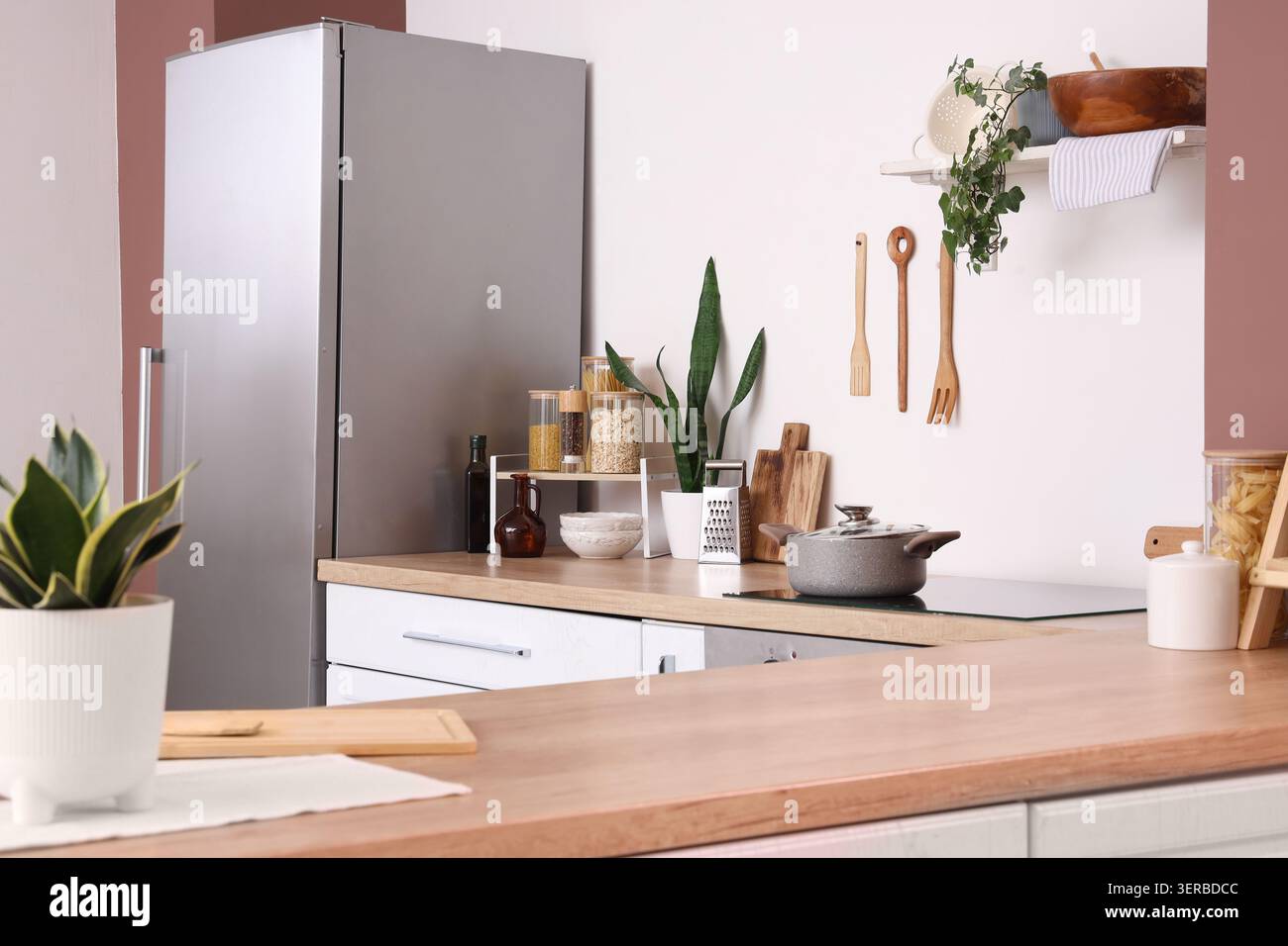 Moderne Küche mit Kühlschrank aus Edelstahl, Holzablageflächen und Kochutensilien Stockfoto