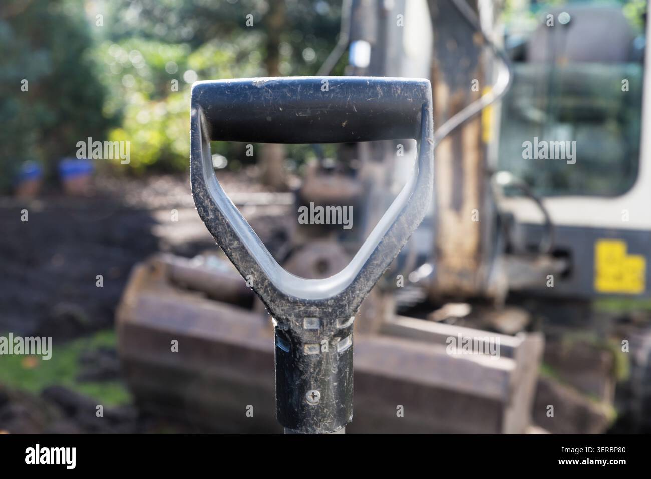 Der Griff einer Schaufel und eines kleinen Schaufelbaggers im Hintergrund Stockfoto