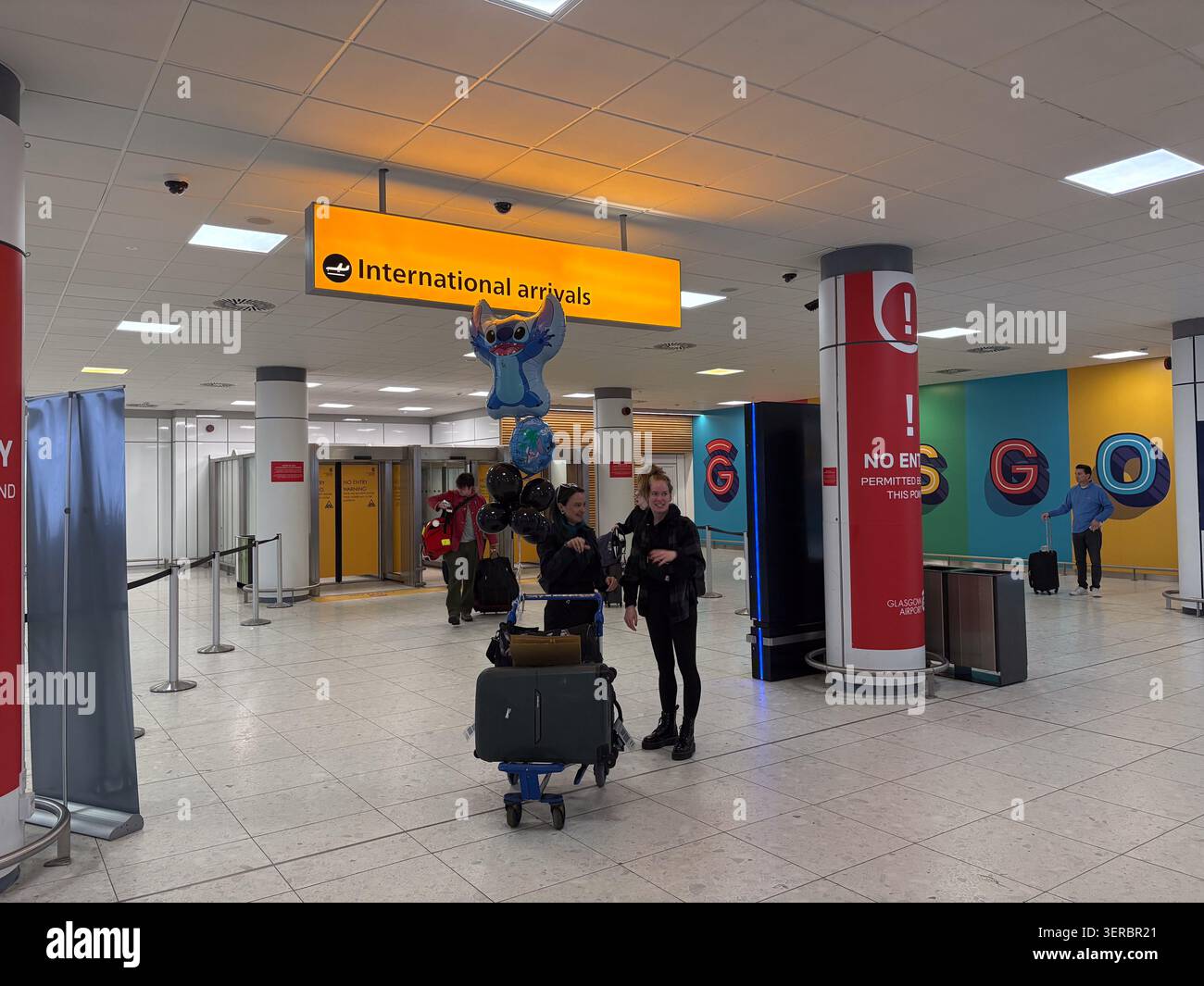 Reisende mit Gepäck und Ballons im internationalen Ankunftsbereich des Glasgow Airport, Schottland, Großbritannien. Stockfoto