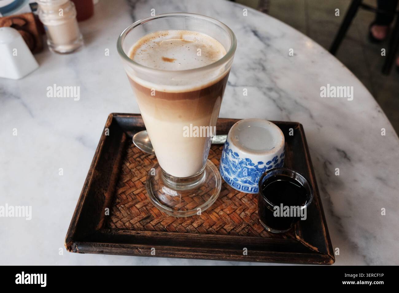 Eiskaffee und heißer schwarzer Kaffee mit Tee auf einem gewebten Tablett auf einem Tisch in einem traditionellen thailändischen Café Shop Stockfoto